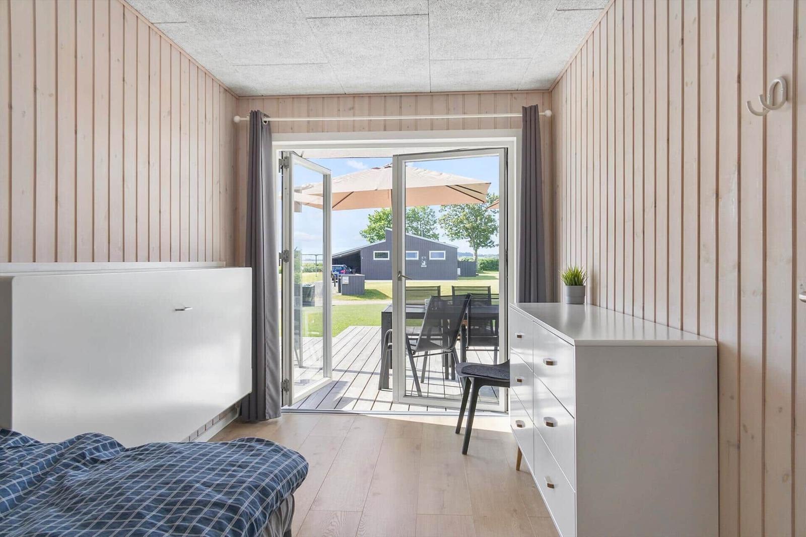 Bedroom with view of terrace and garden. Wooden walls, white furniture, and sliding door.