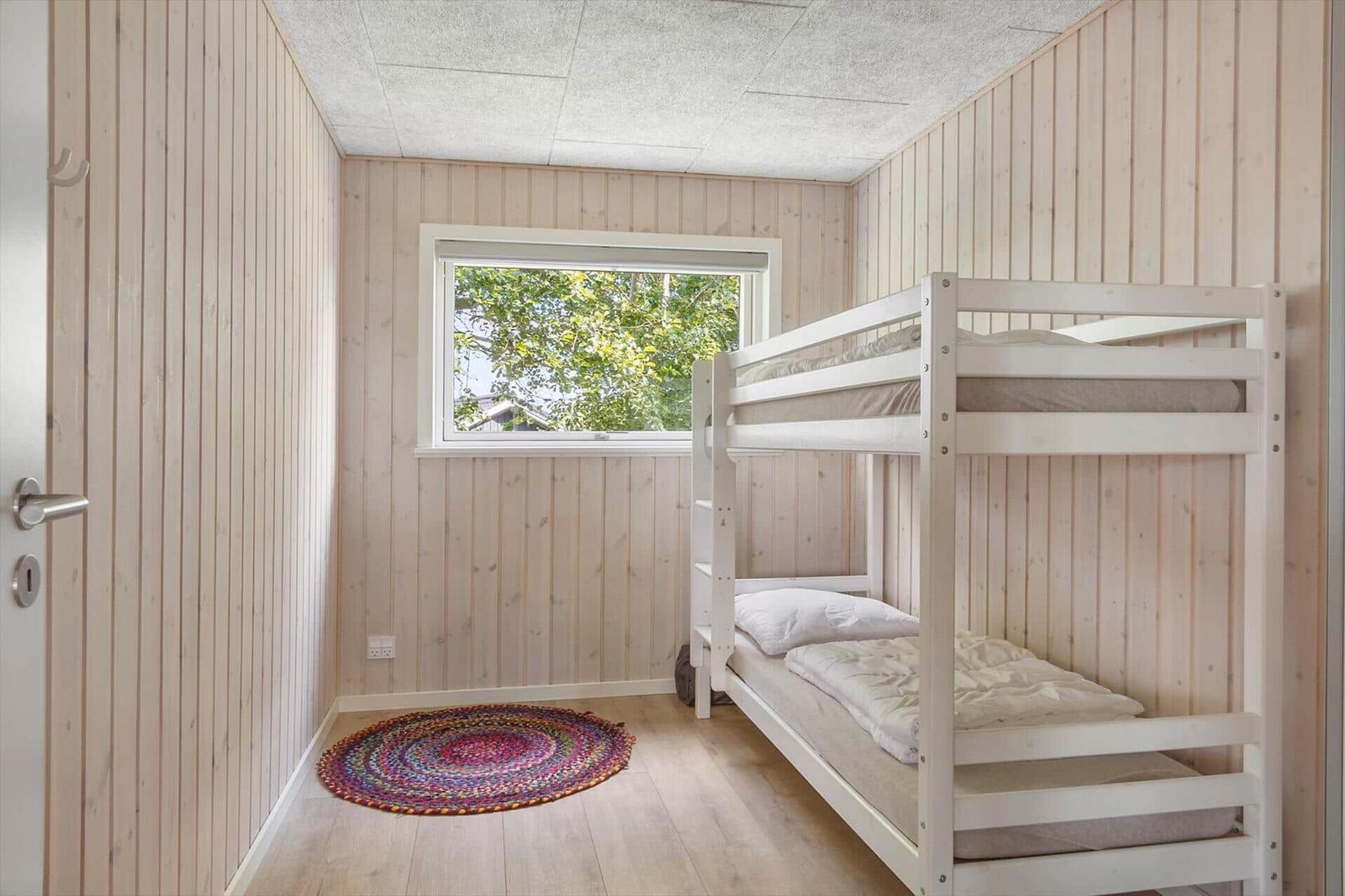 Room with bunk bed, wood-paneled walls, and window with view of trees.