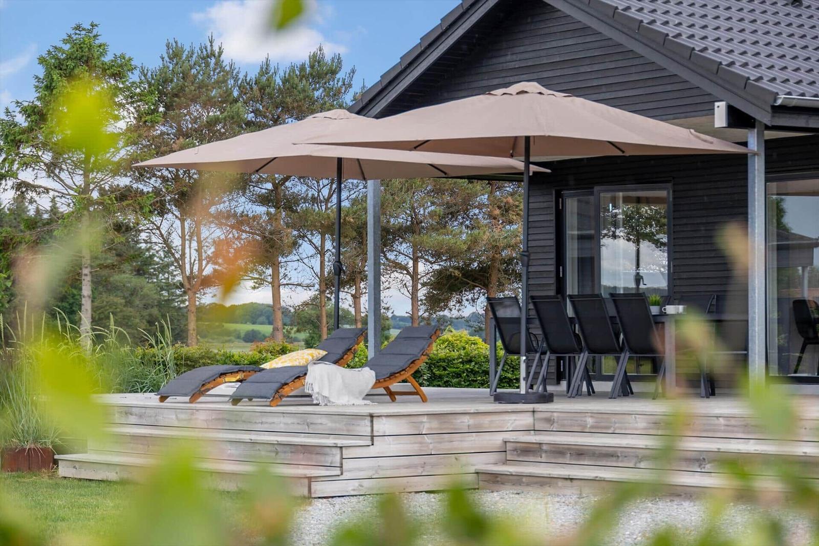 Deck with lounge chairs, umbrellas, and seating area in front of a house with glass doors.