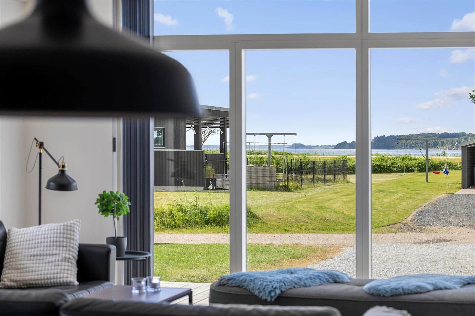 Large window with view of garden and water. Black lamp and sofa in foreground.