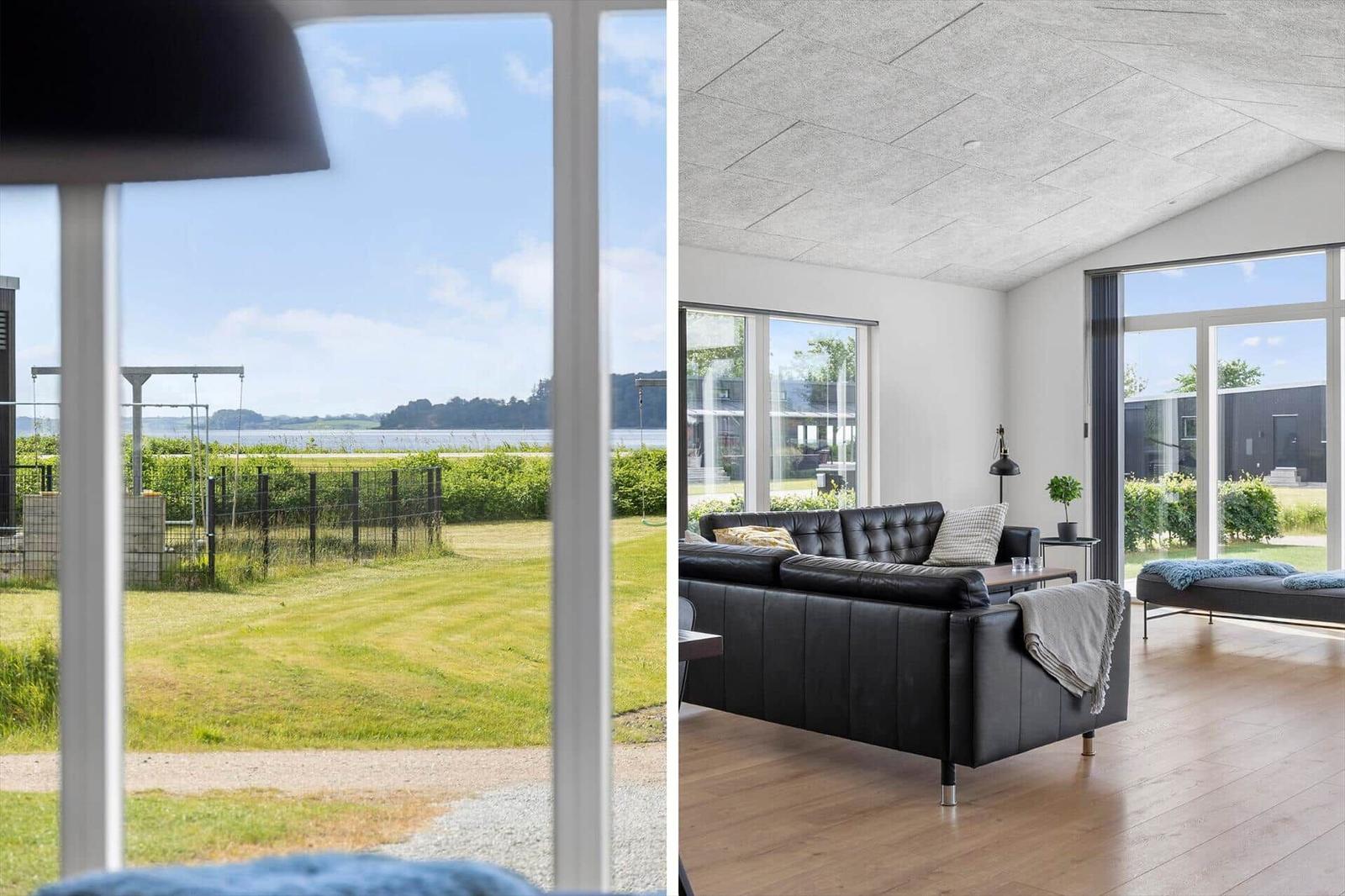 Living room with black leather sofa and wooden floor. Outside: grass field and water visible.