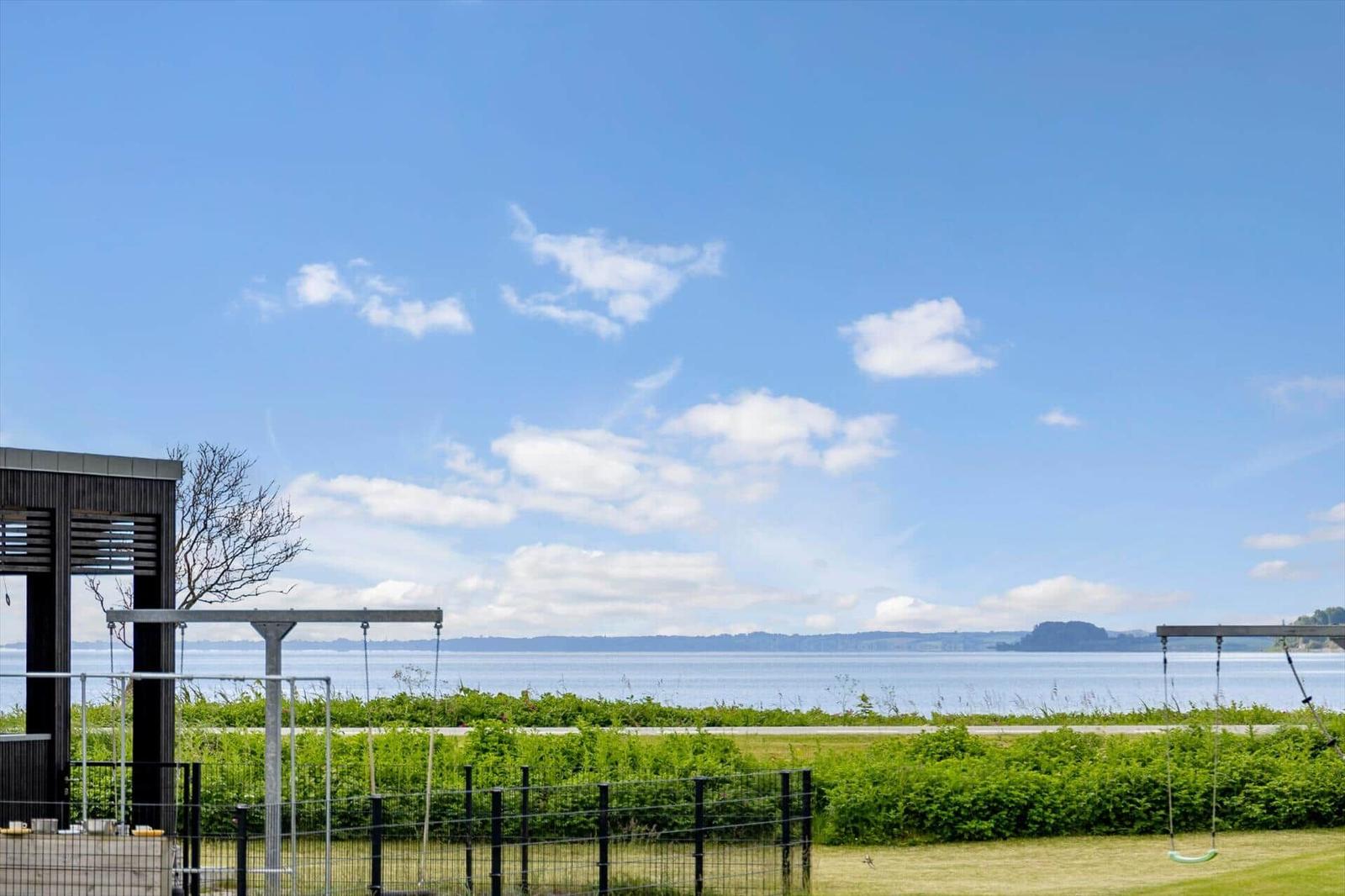 Outdoor area with view of lake and sky. Play equipment and fence are visible.