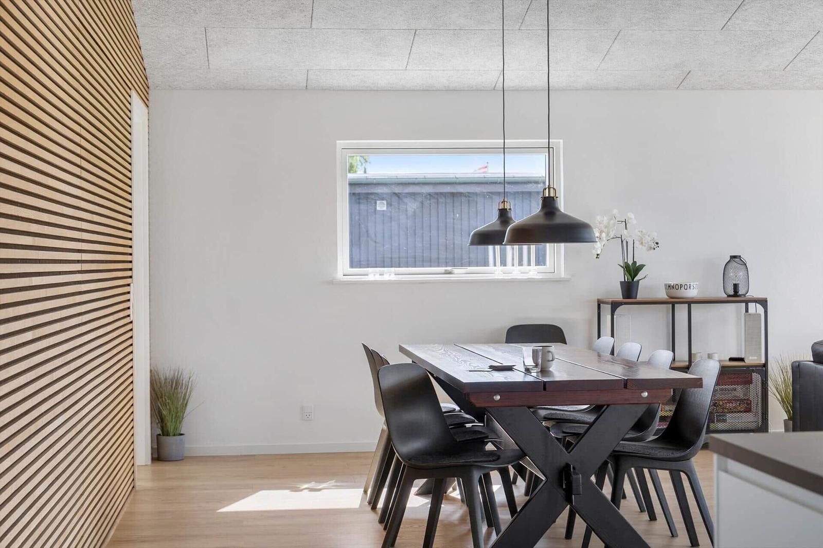 Dining room with table, chairs, and window. Wooden wall and pendant lamps.