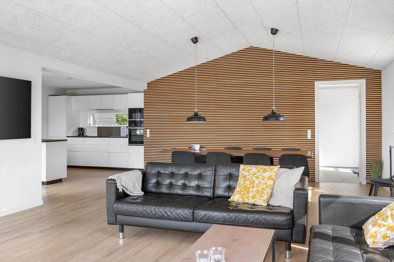 Living and dining area with black leather sofa and wooden wall. Kitchen in background.
