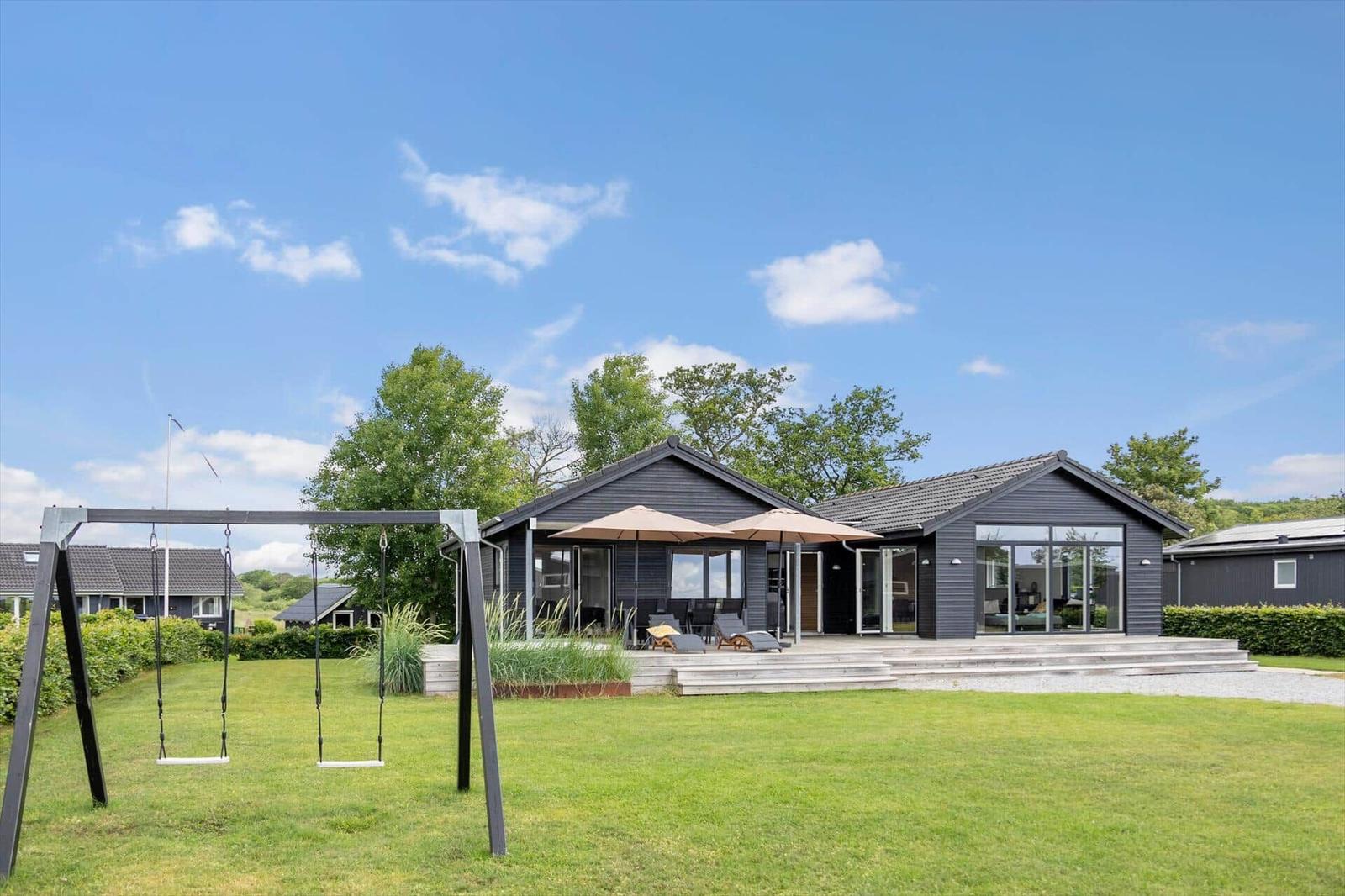 Modern villa with terrace, garden, and swing under blue sky.