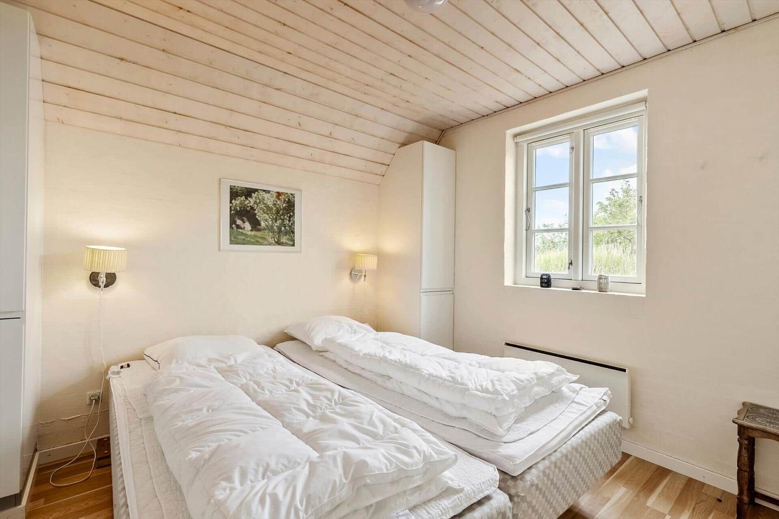 Zwei Betten mit weißen Bettwäschen, Fenster mit Blick auf Grün, Holzdecke und Wandlampen.