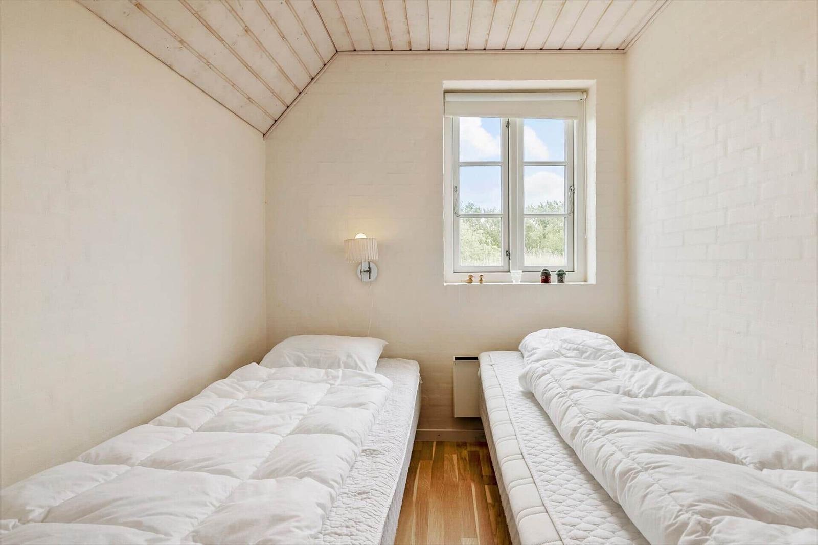 Zwei Betten mit weißen Bettwäsche, Fenster und Wandlampe in einem Raum mit Holzboden.