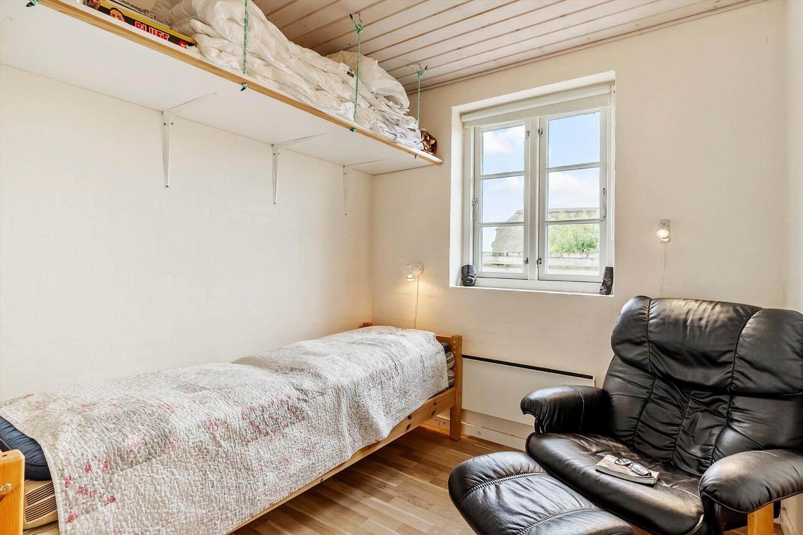 Ein Zimmer mit einem Bett, einem schwarzen Ledersessel und einem Fenster.