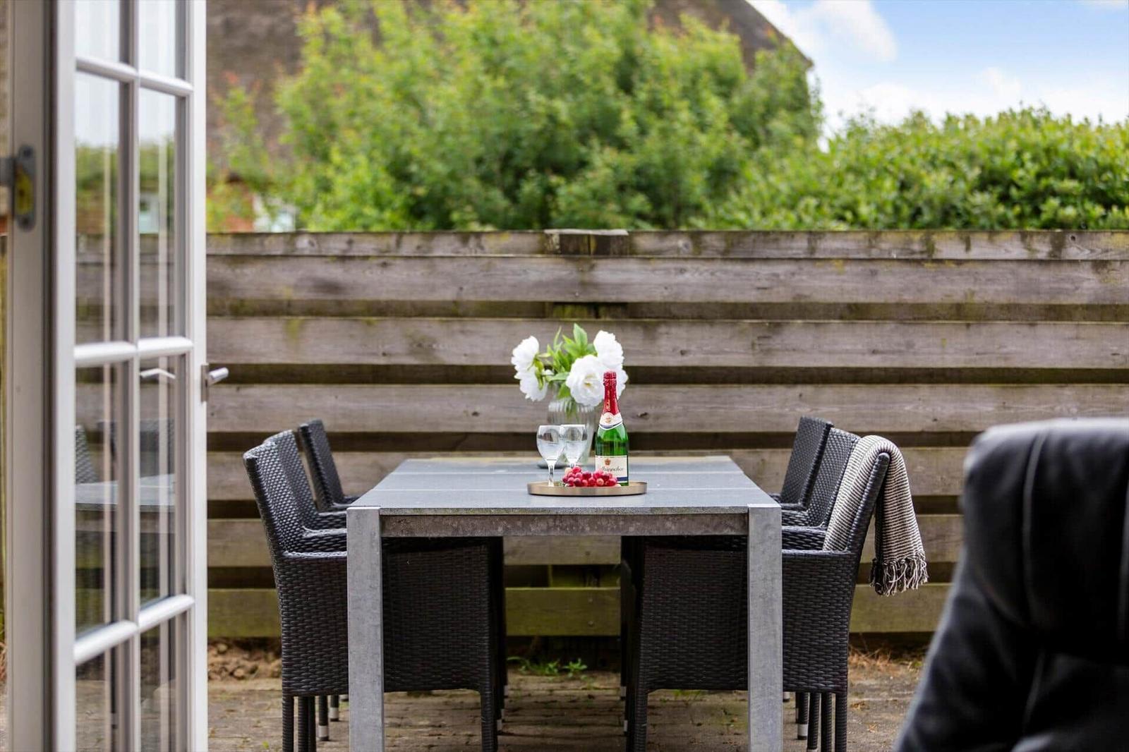 Terrasse mit Tisch, Stühlen, Blumen und einer Flasche Sekt.