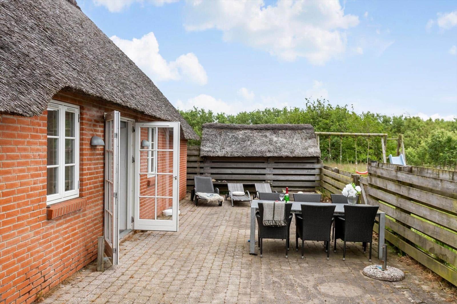 Haus mit strohgedecktem Dach, Terrasse mit Tisch, Stühlen und Liegestühlen.