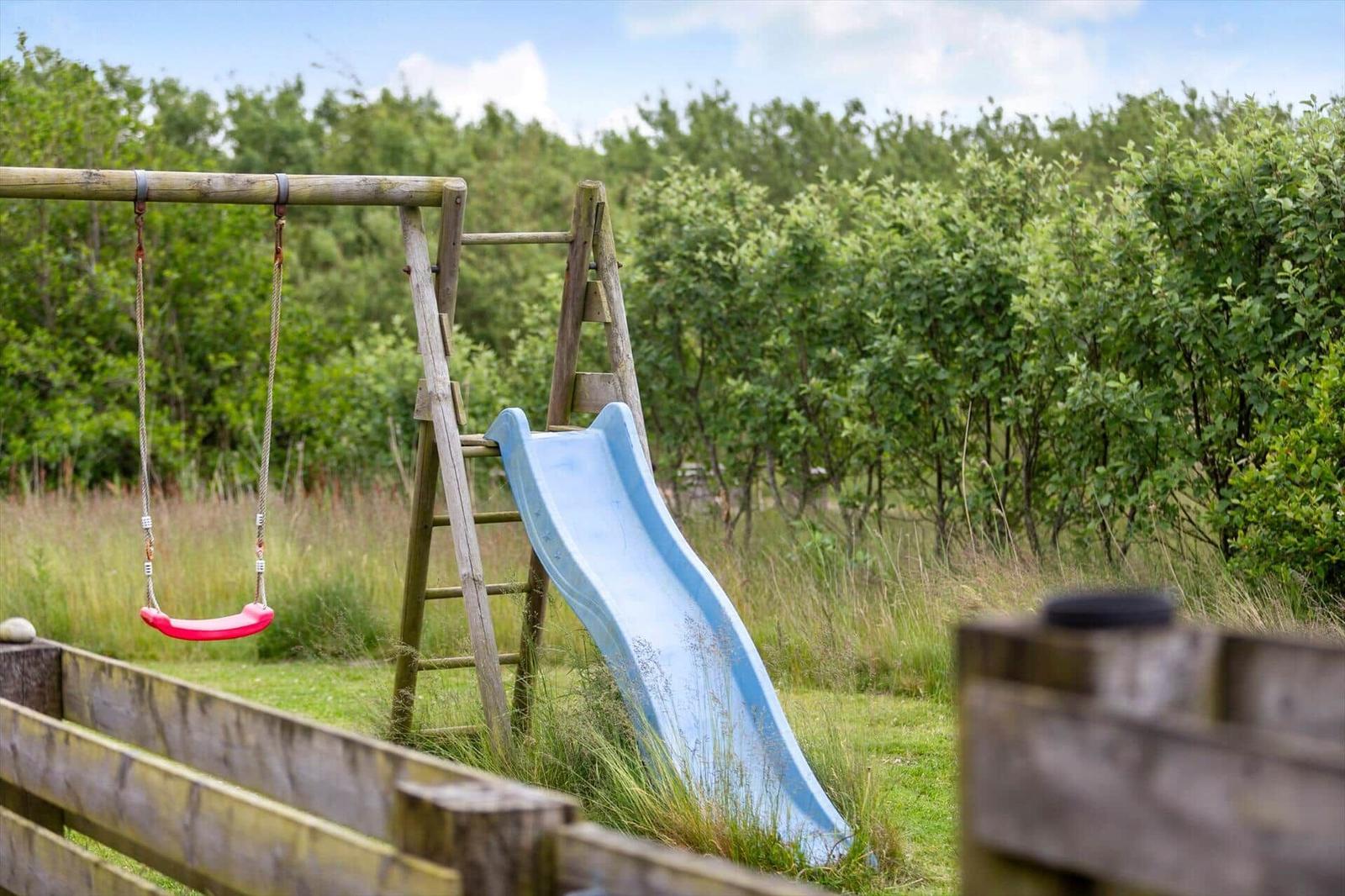 Holzspielplatz mit Rutsche und Schaukel im Grünbereich.