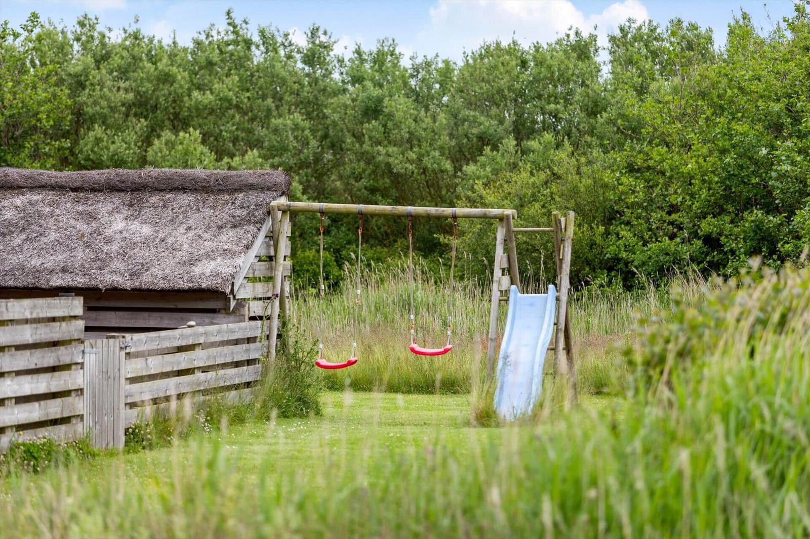 Hinterhof mit Schaukel und Rutsche neben einem Strohdachhaus.