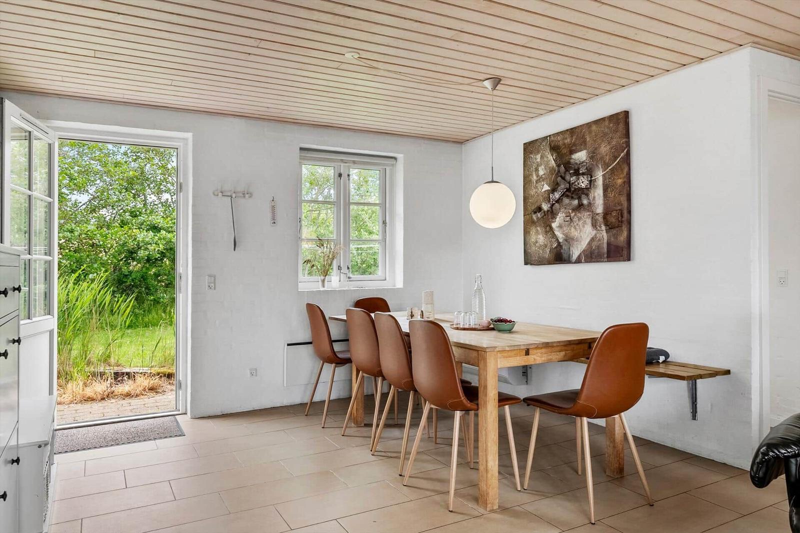 Esszimmer mit Holztisch, braunen Stühlen und Fenster zur grünen Außenterrasse.