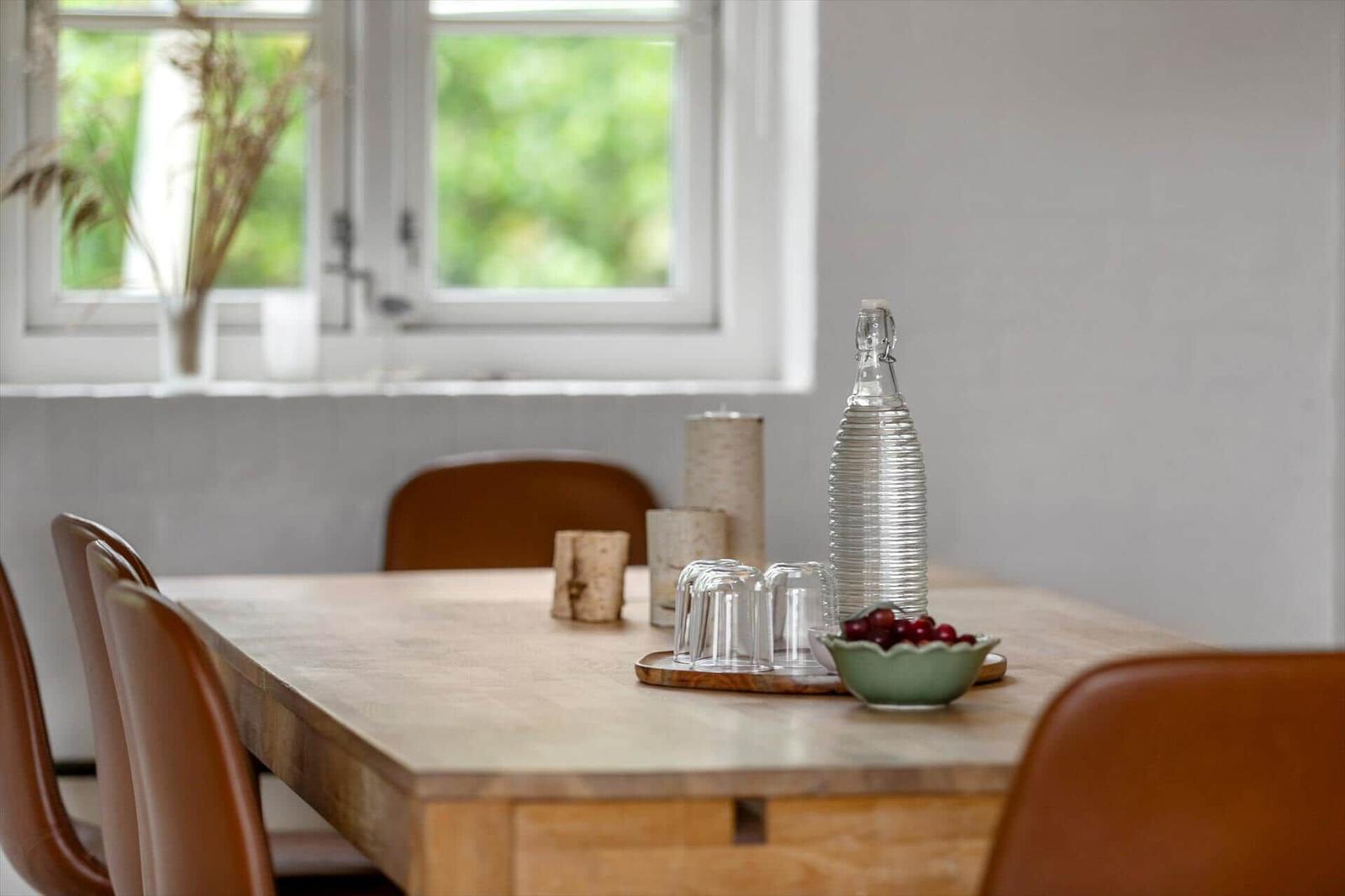 Holztisch mit Stühlen, Wasserflasche und Beeren auf der Fensterbank.