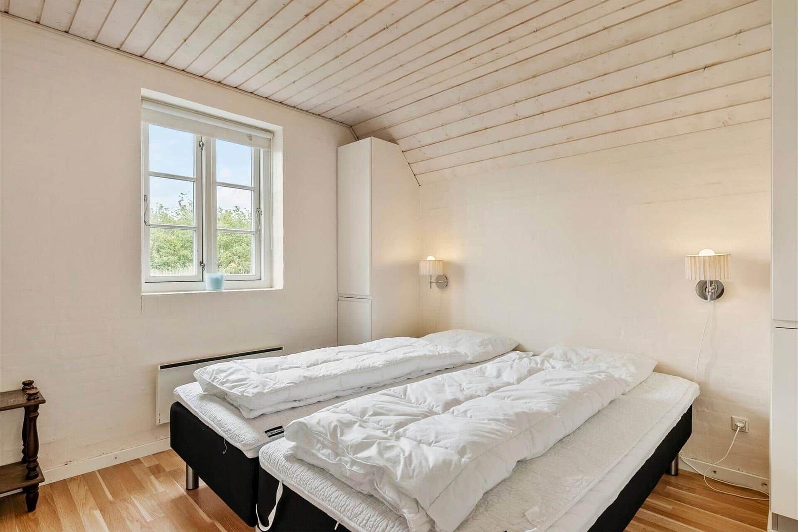 Schlafzimmer mit Doppelbett, Fenster und Holzboden. An der Wand hängen zwei Lampen.