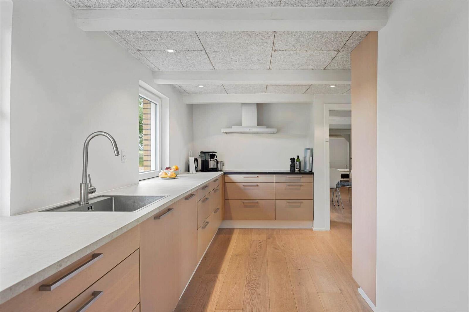 Modern kitchen with wooden floor and light cabinets. Window, sink, and range hood visible.