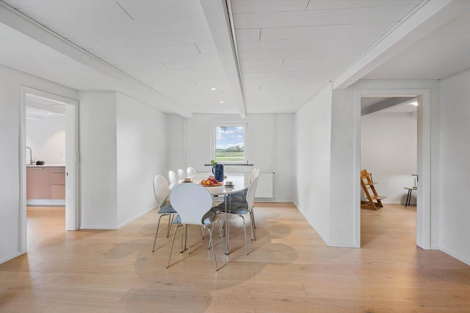Dining area with table and chairs, view of garden. Kitchen and bedroom are visible.