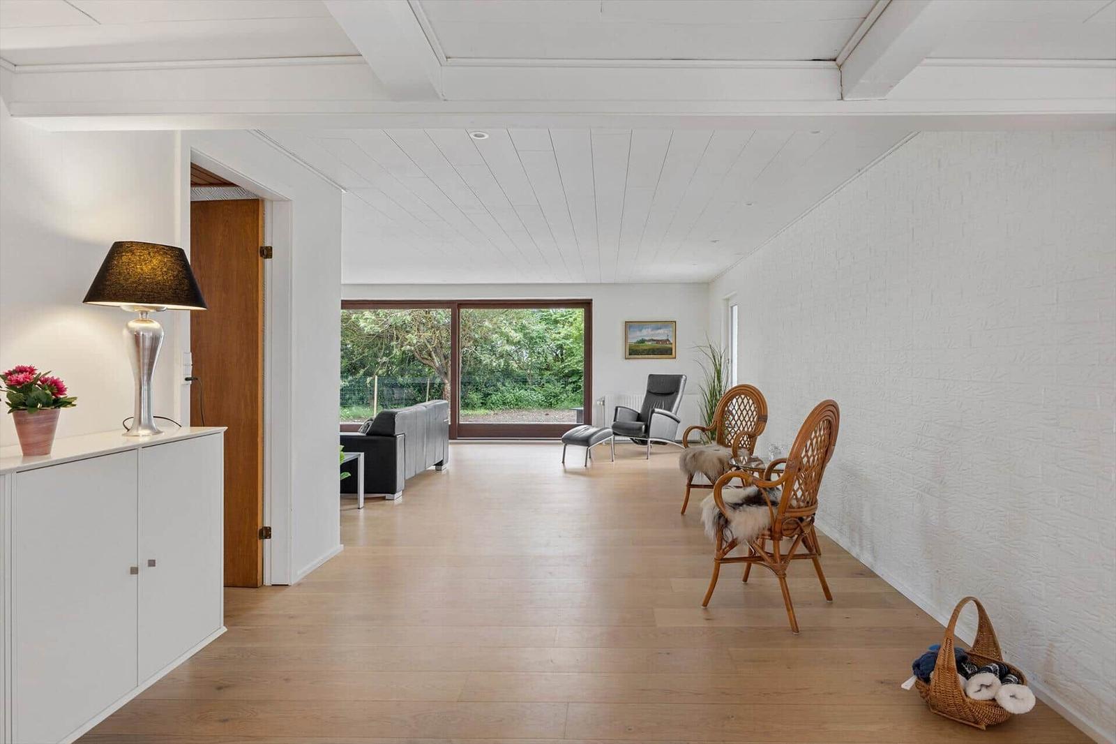 Entrance area with white walls, wooden floor, and seating. Corridor to living room with garden view.
