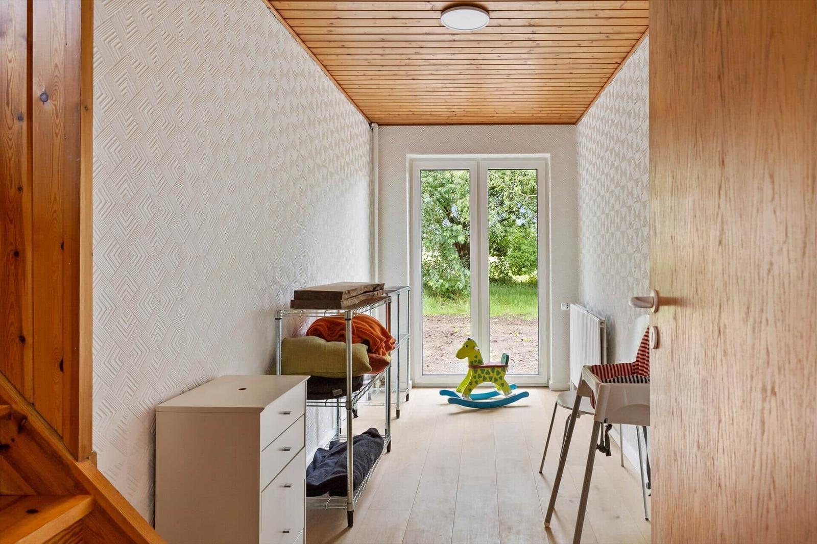 A room with wooden ceiling, window to garden, and childs rocking horse.