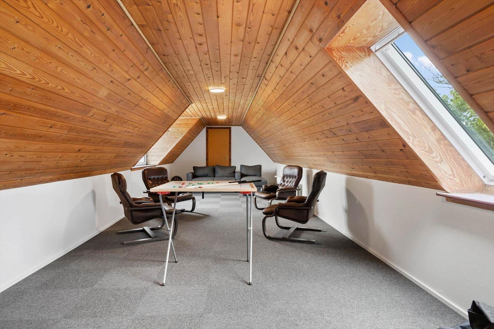 Attic room with wooden ceiling, table, four chairs, and sofa. Large skylight.