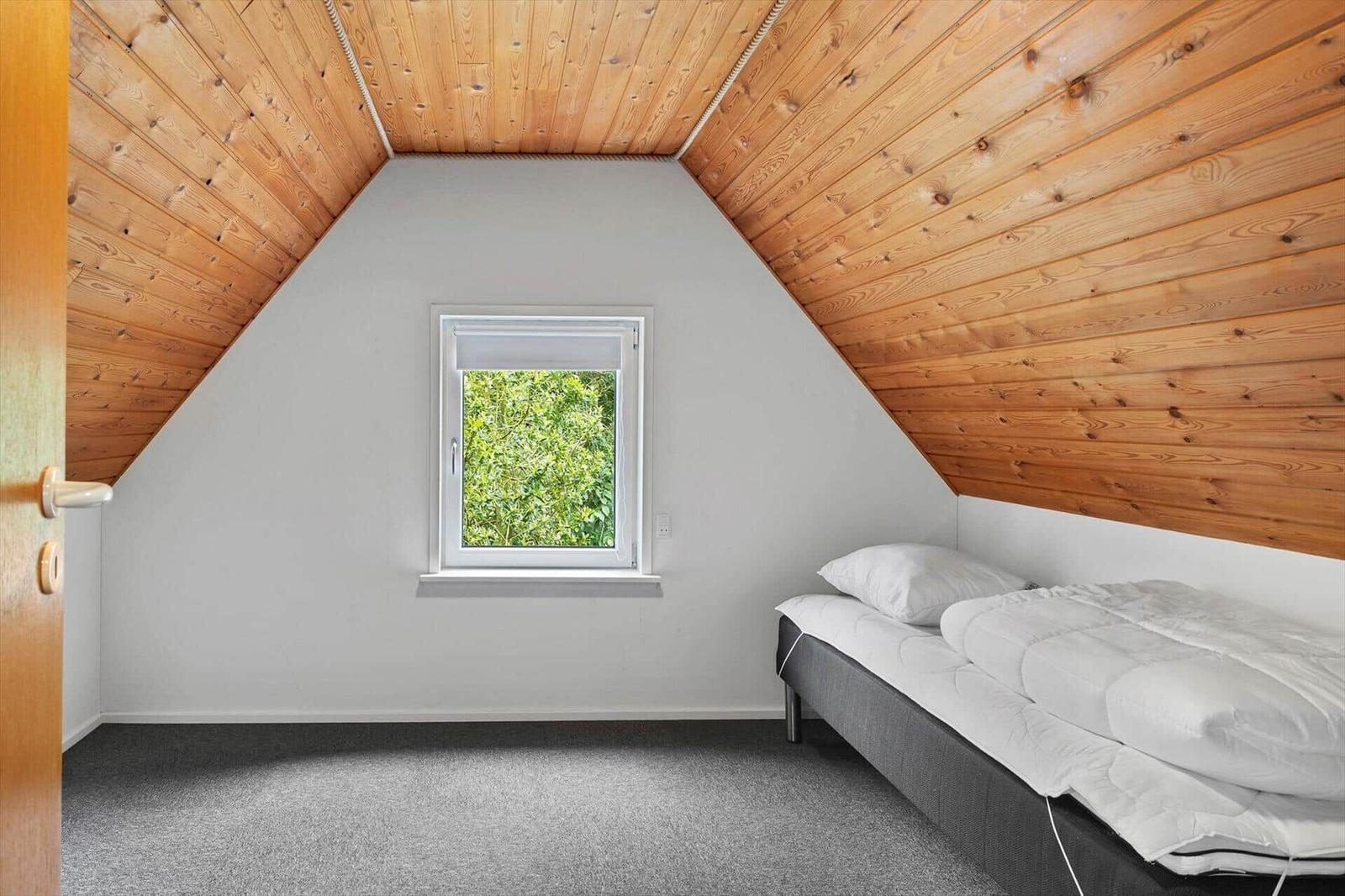 Bedroom with wooden ceiling, window, and bed.