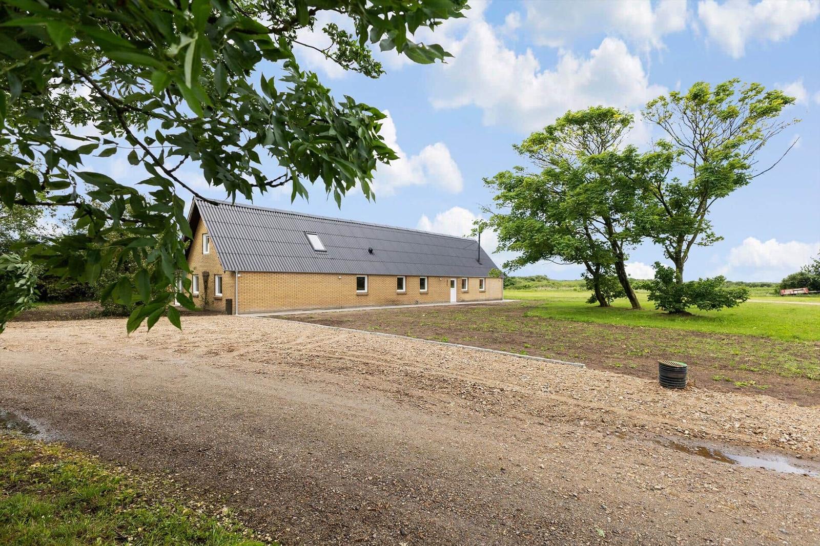 A long house with brown walls and gray roof stands on a green lawn.