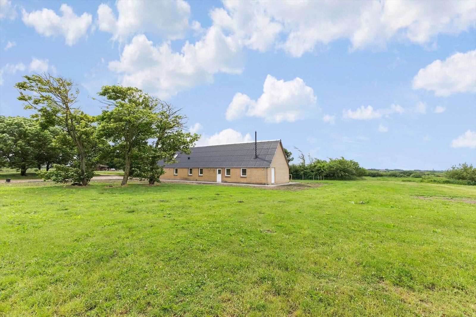 A modern house with a roof and windows stands on a green lawn under a blue sky.