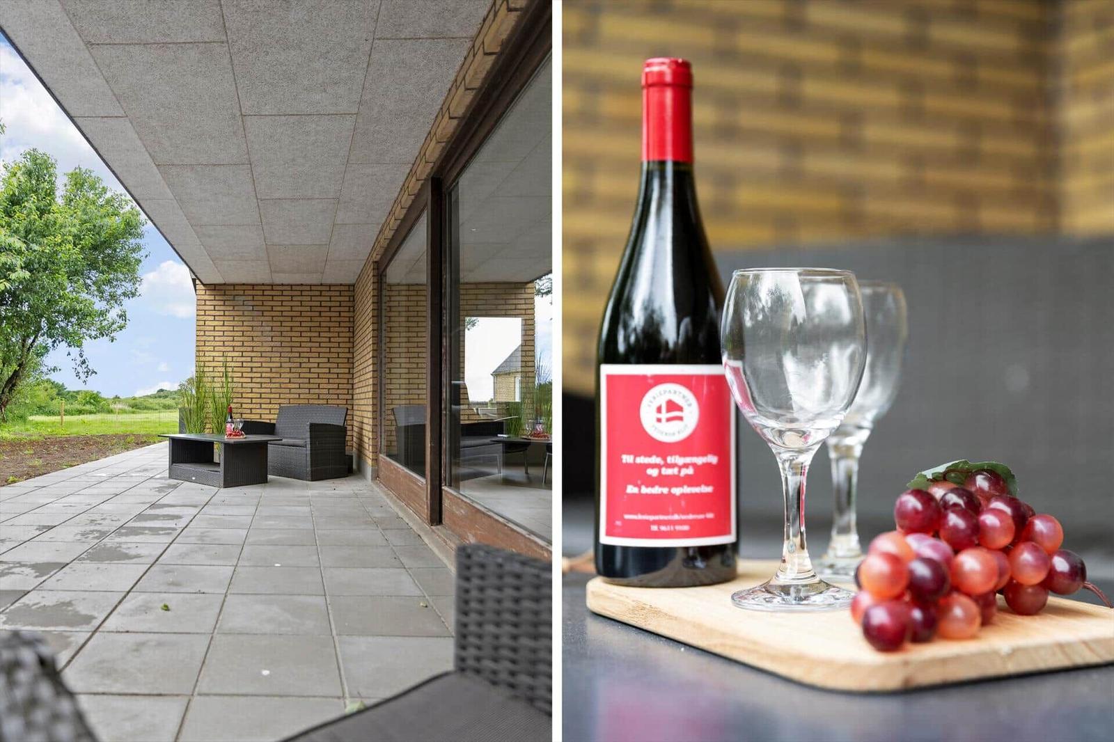 Terrace with seating and green field view. Wine bottle, glasses, and grapes on table.