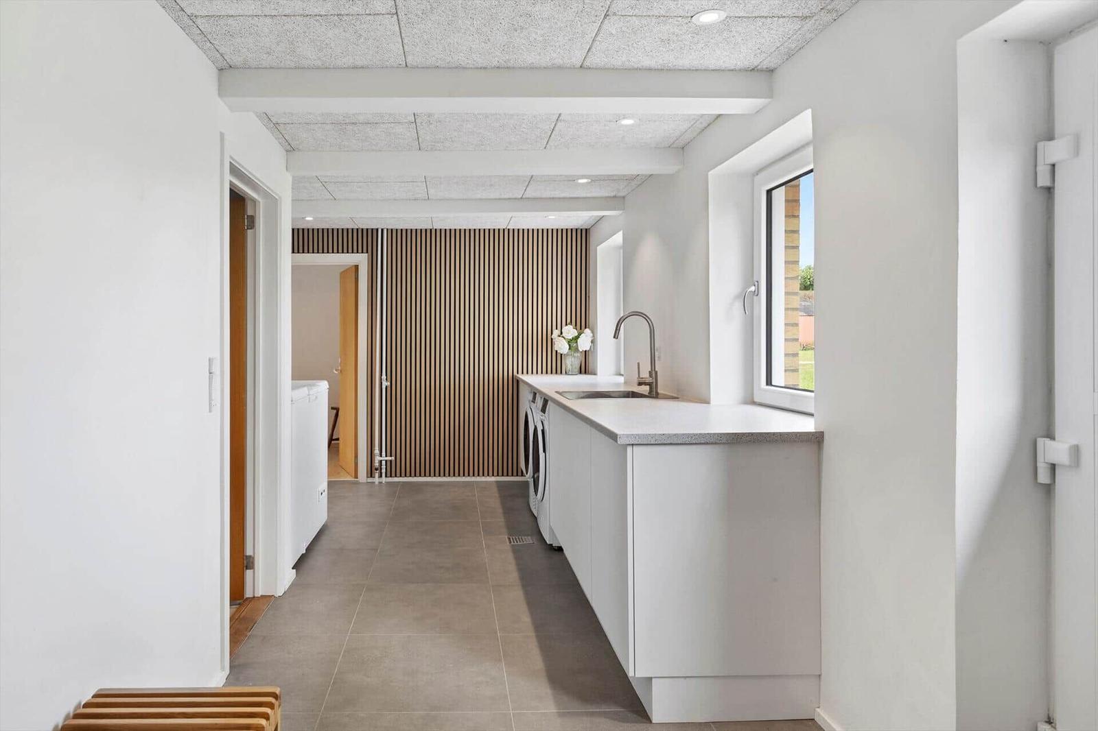 Kitchen with washing machine and window. Wooden wall in background.