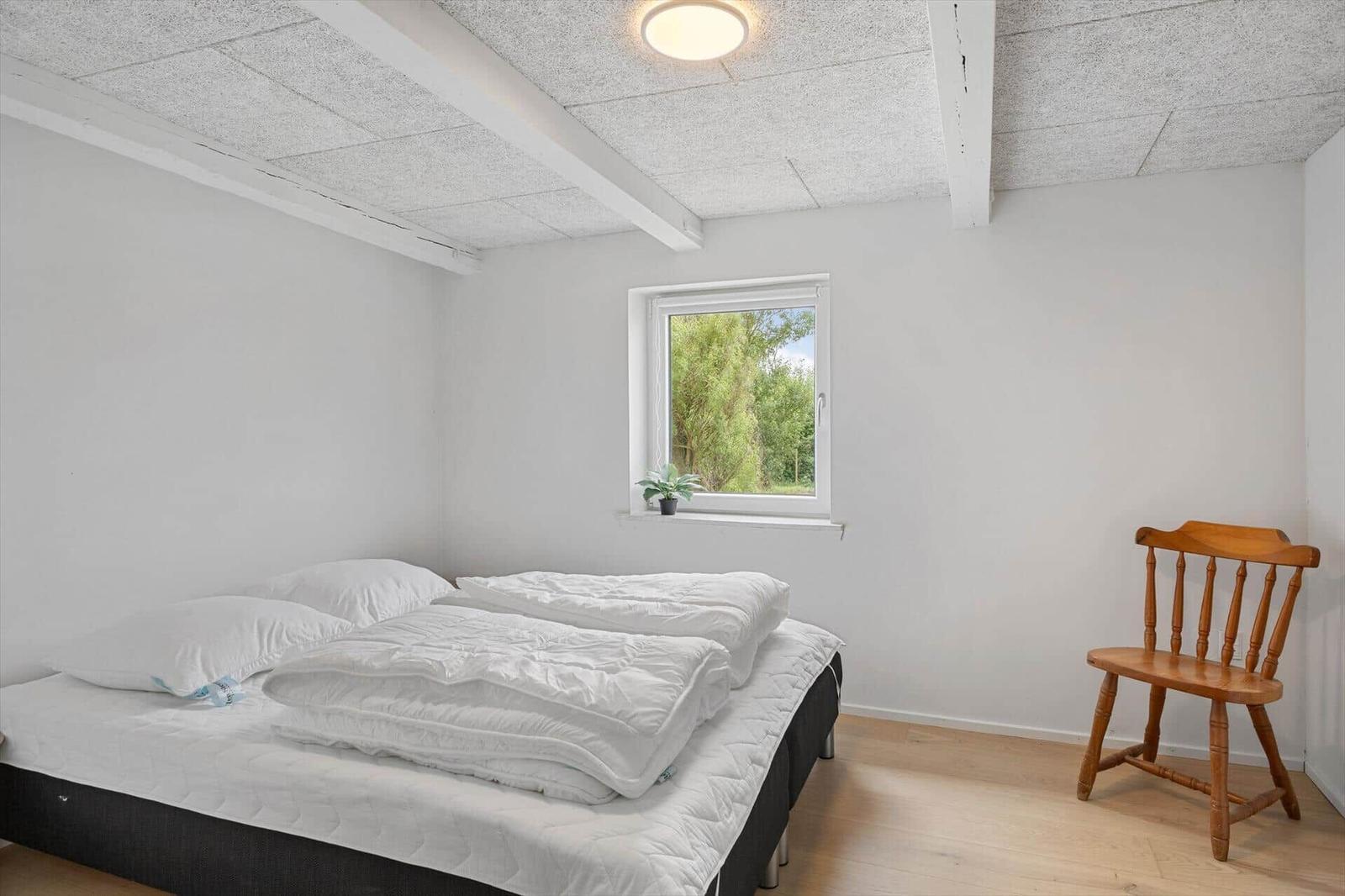 Bedroom with bed, chair, and window. Ceiling with beams.