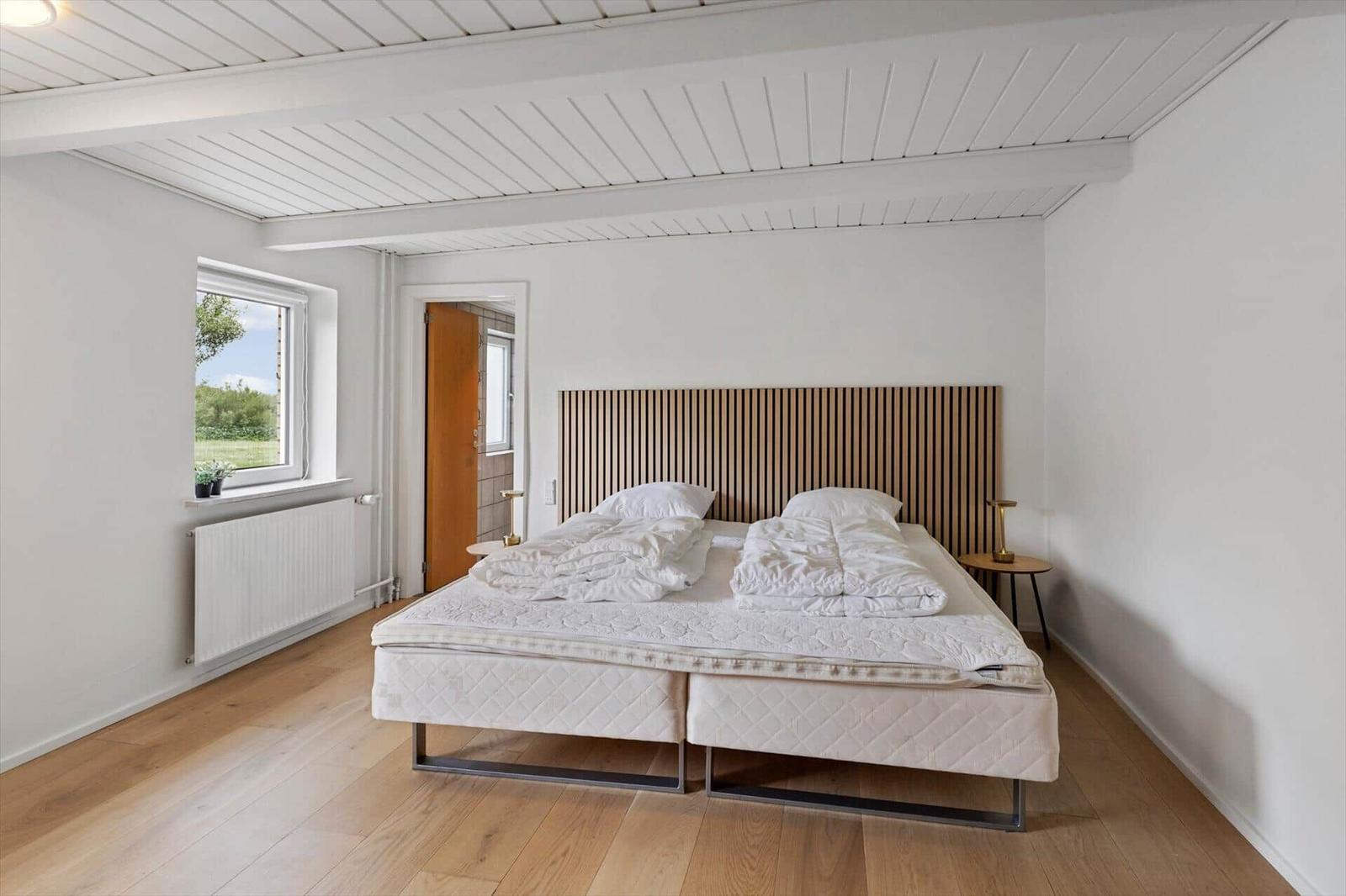 Bedroom with double bed, wooden floor, and window with view of green area.