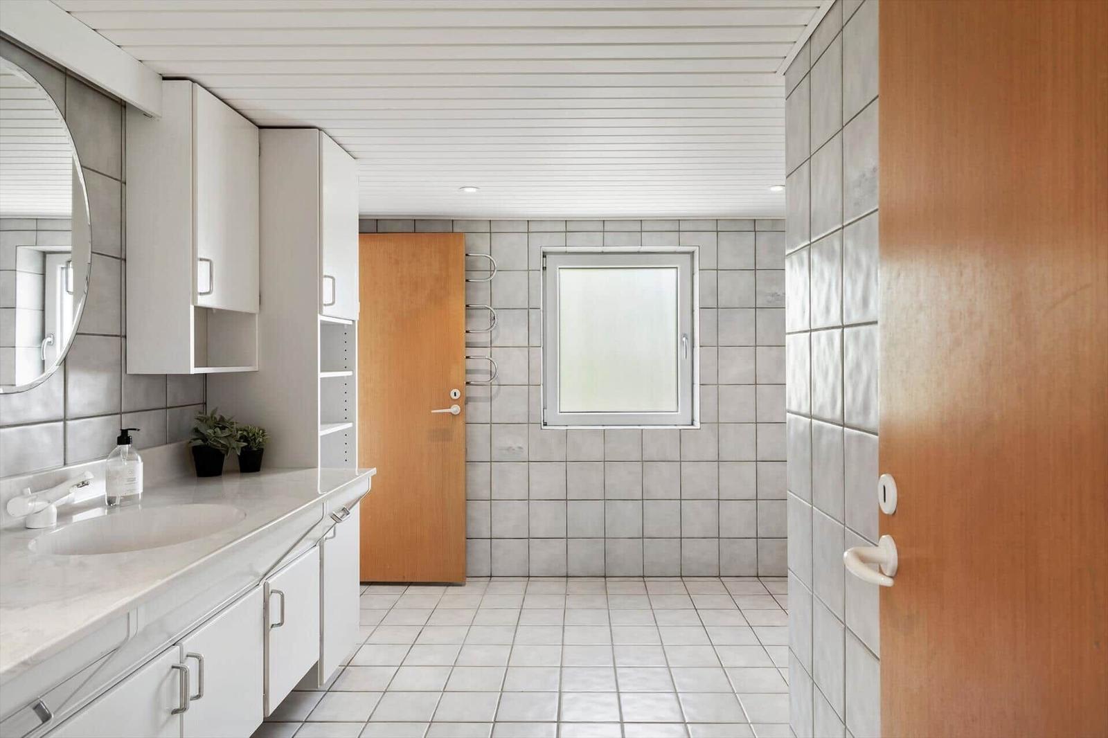 Bathroom with sink, mirror, and window. Tiles on walls and floor.