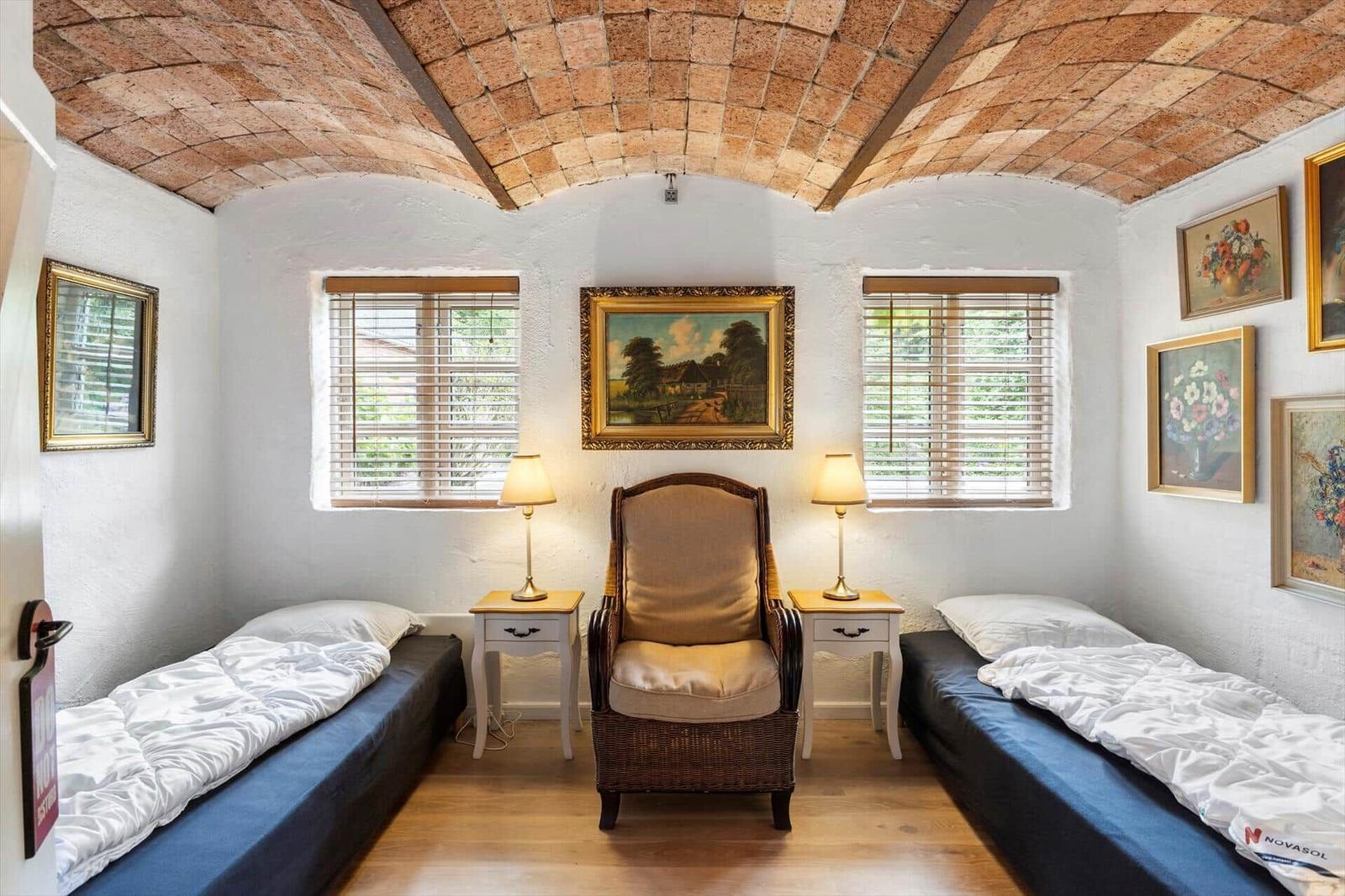 Zimmer mit zwei Betten, Sessel und Steinbogendecke. Fenster mit Jalousien und Wandbilder.