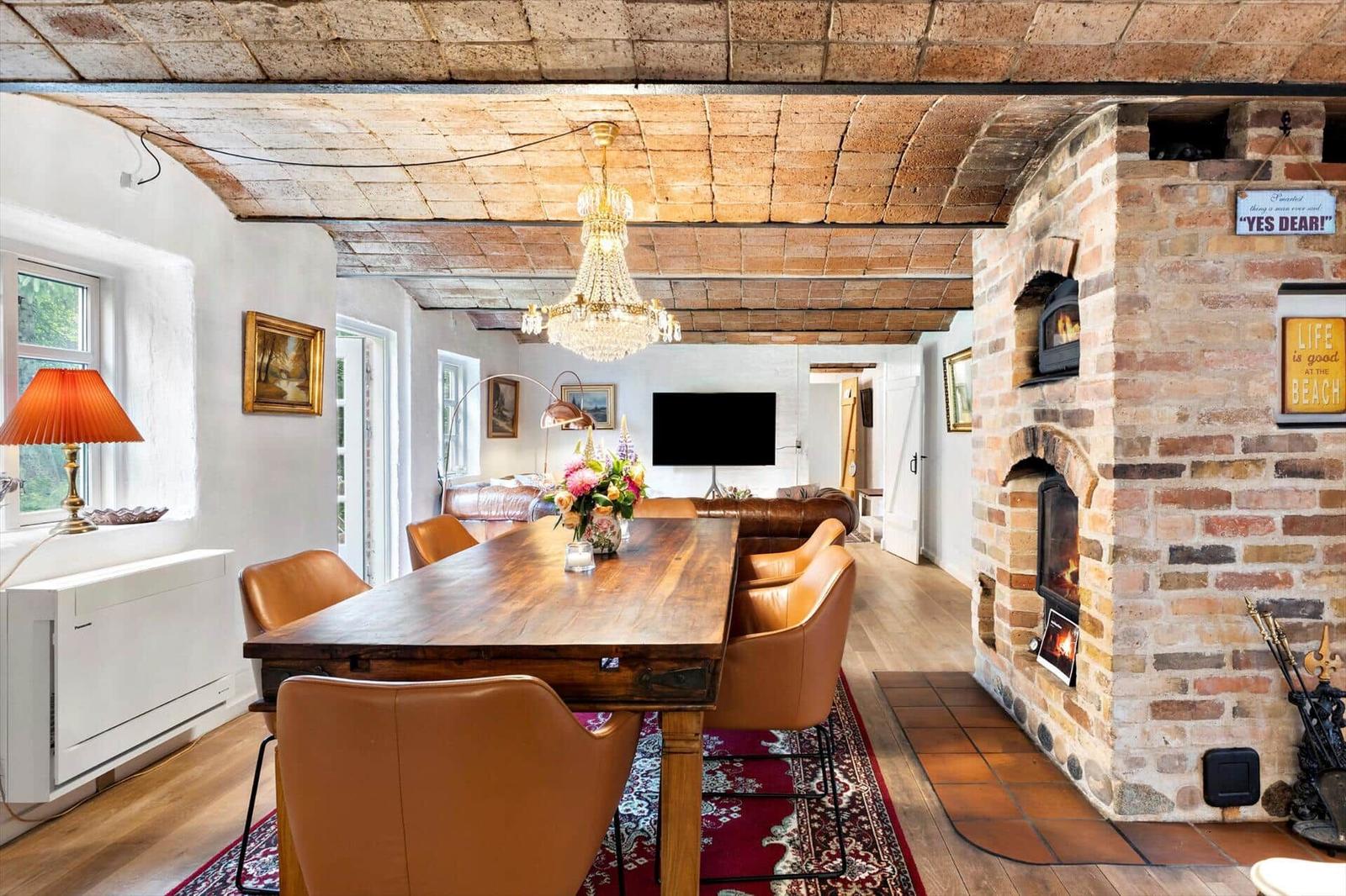 Esszimmer mit Holztisch, Ledersitzen und Steinofen an der Wand.