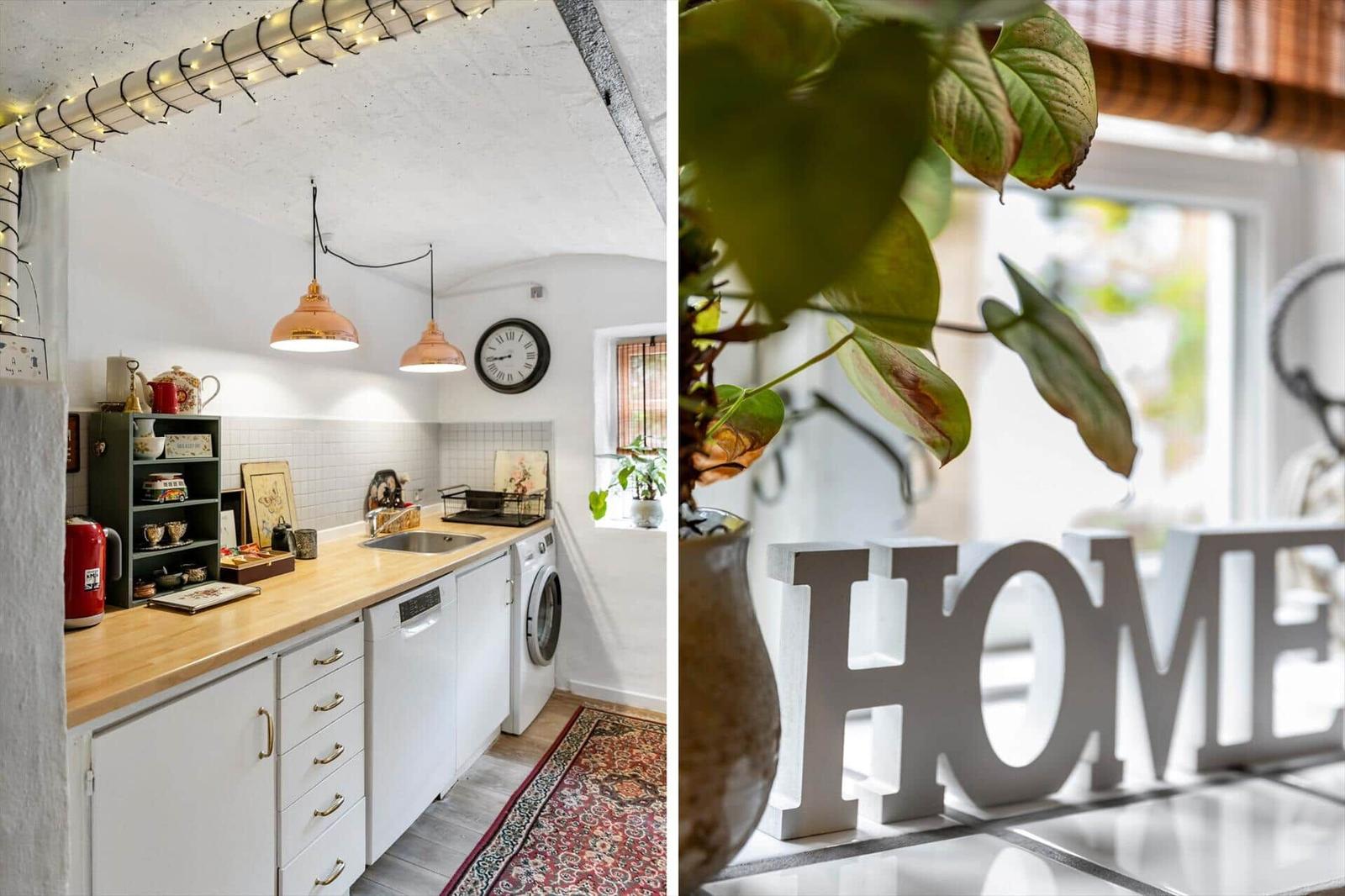 Küche mit Holz Arbeitsplatte und weißen Schränken. Wohnbereich mit Pflanze und HOME-Schild.