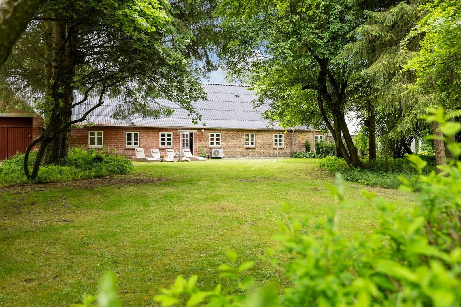 Rotes Backsteingebäude mit grünem Garten und Liegestühlen unter Bäumen.