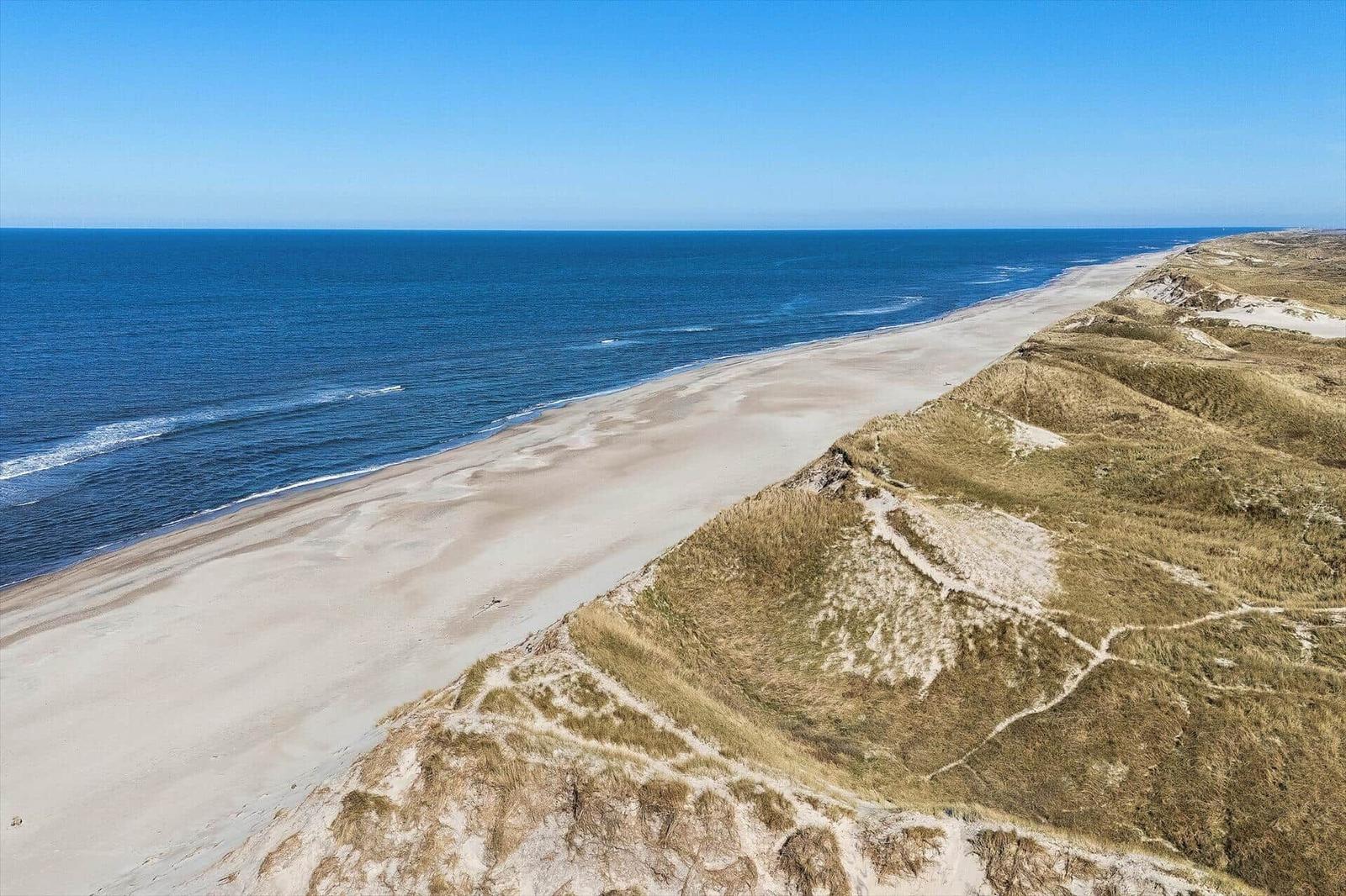 Aerial view of a sandy beach next to dunes and the blue sea.