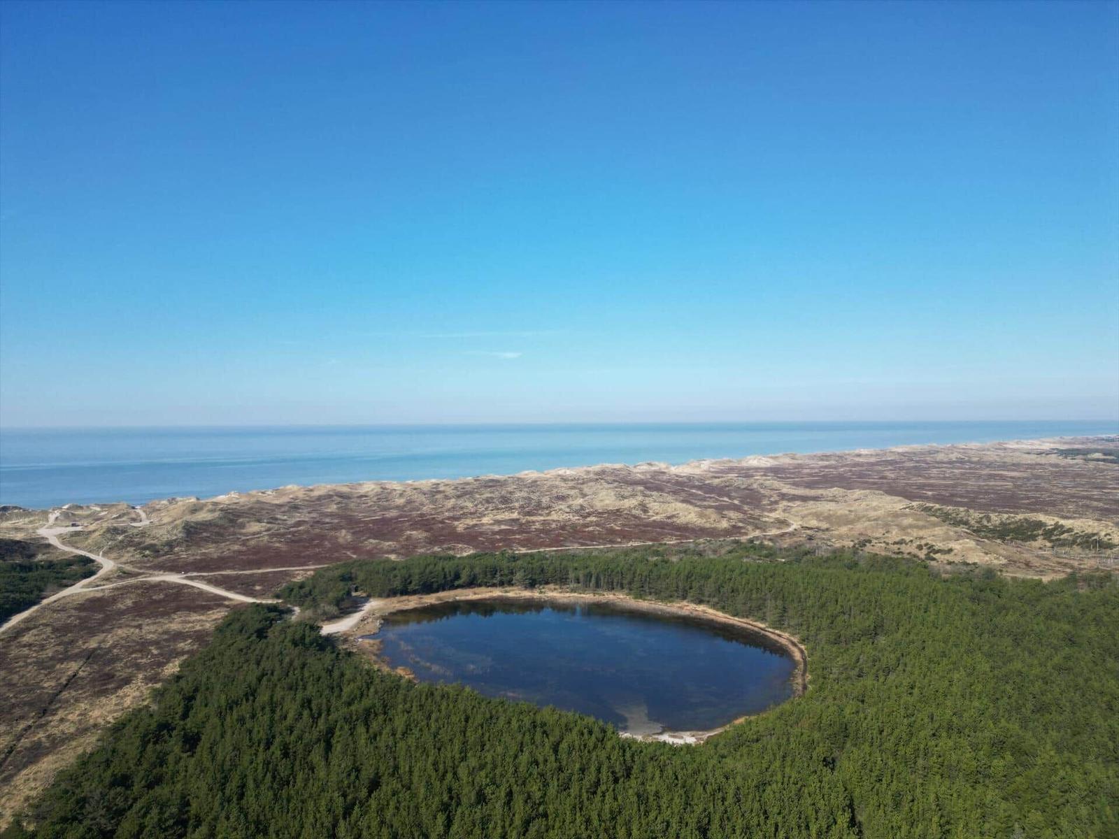 A circular lake is surrounded by a forest, hills, and the sea.