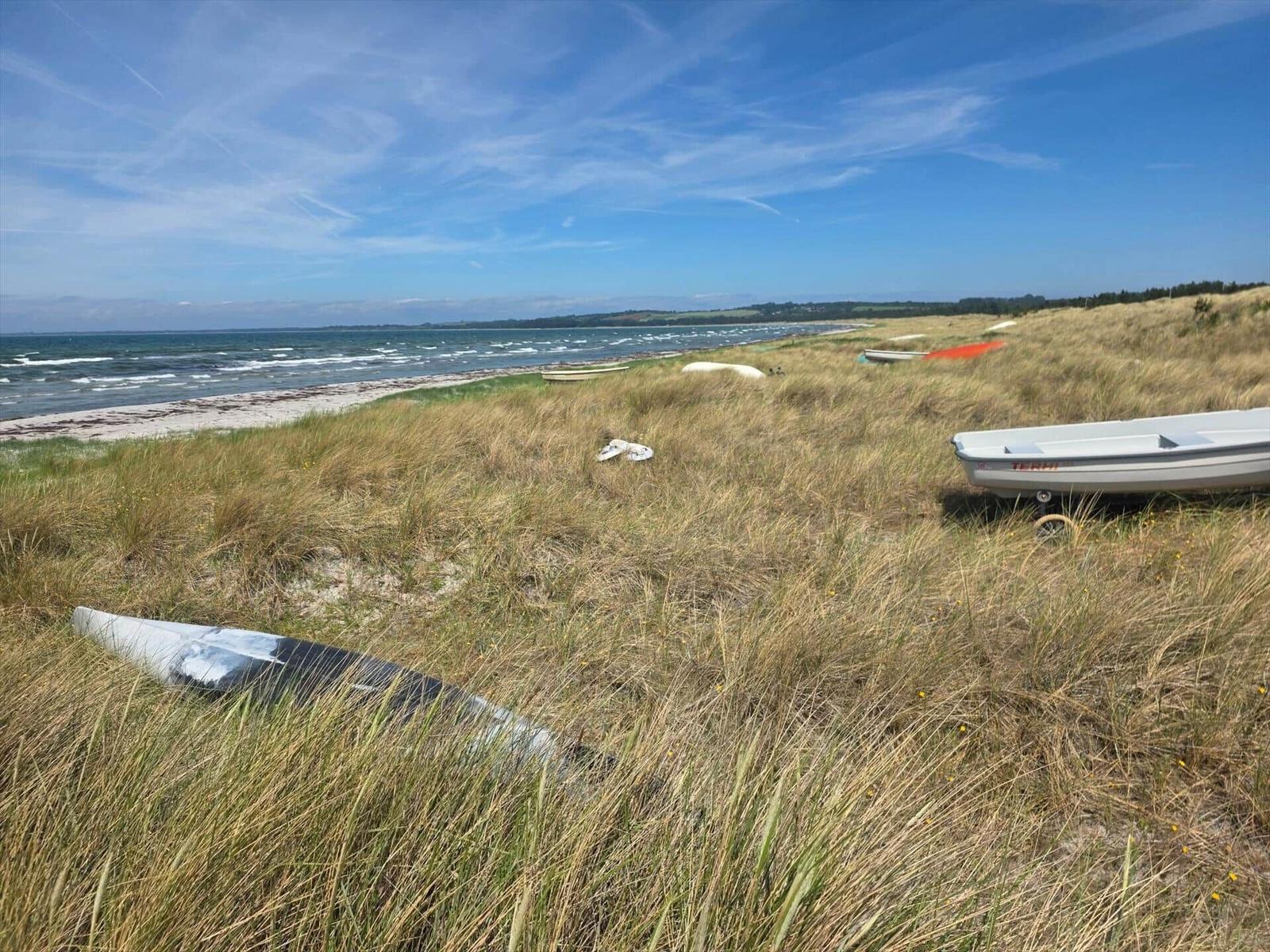 Strand mit Segelbooten und Grashügeln unter blauem Himmel