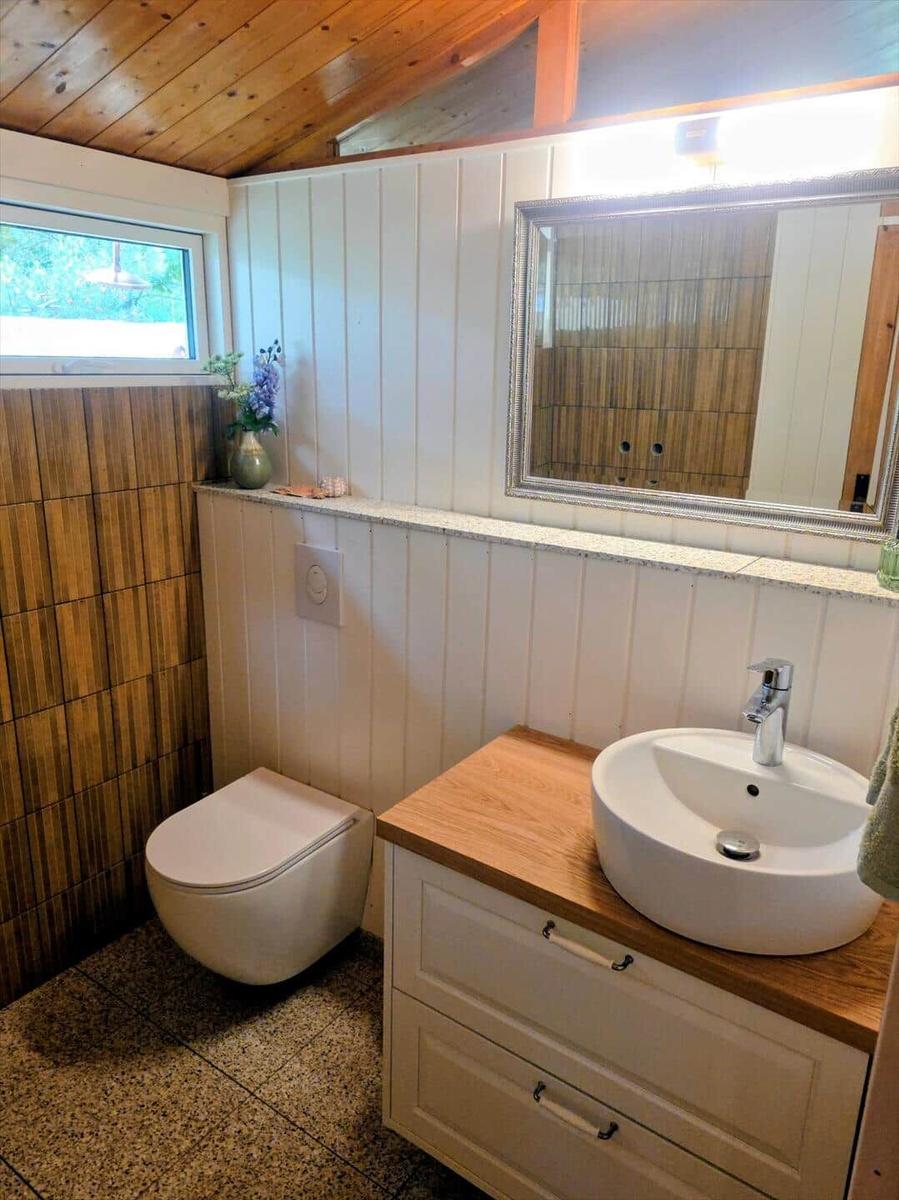 Badezimmer mit Waschbecken, Spiegel und Toilette unter Holzdecke.