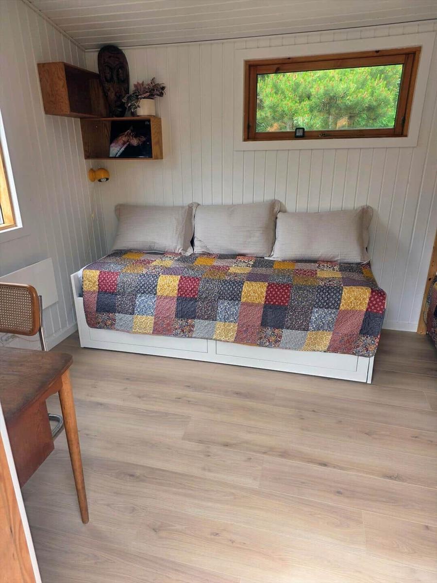 Schlafzimmer mit Bett, Decke und Fenster. Holzfußboden und Wandregale.