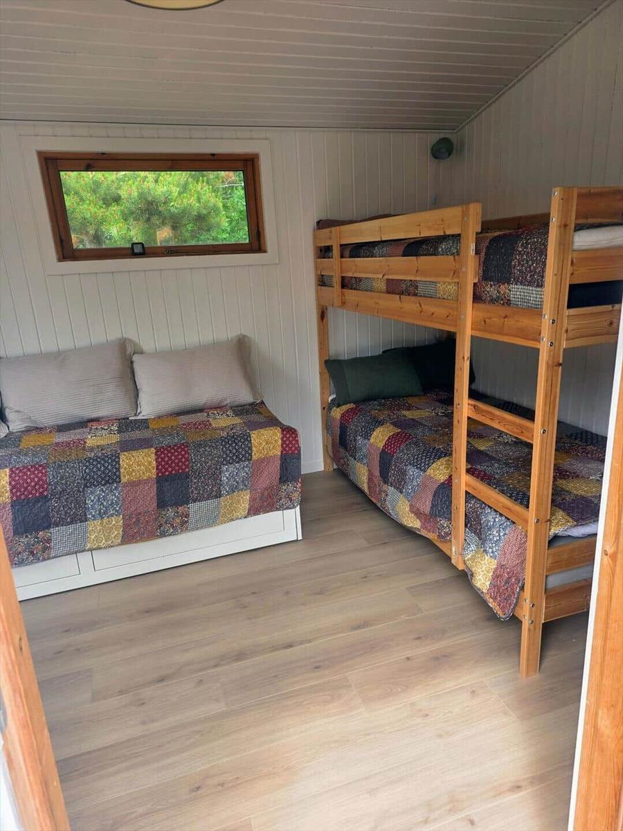 Zimmer mit Etagenbett und Schlafcouch, Holzfußboden und Fenster mit Blick auf Bäume.