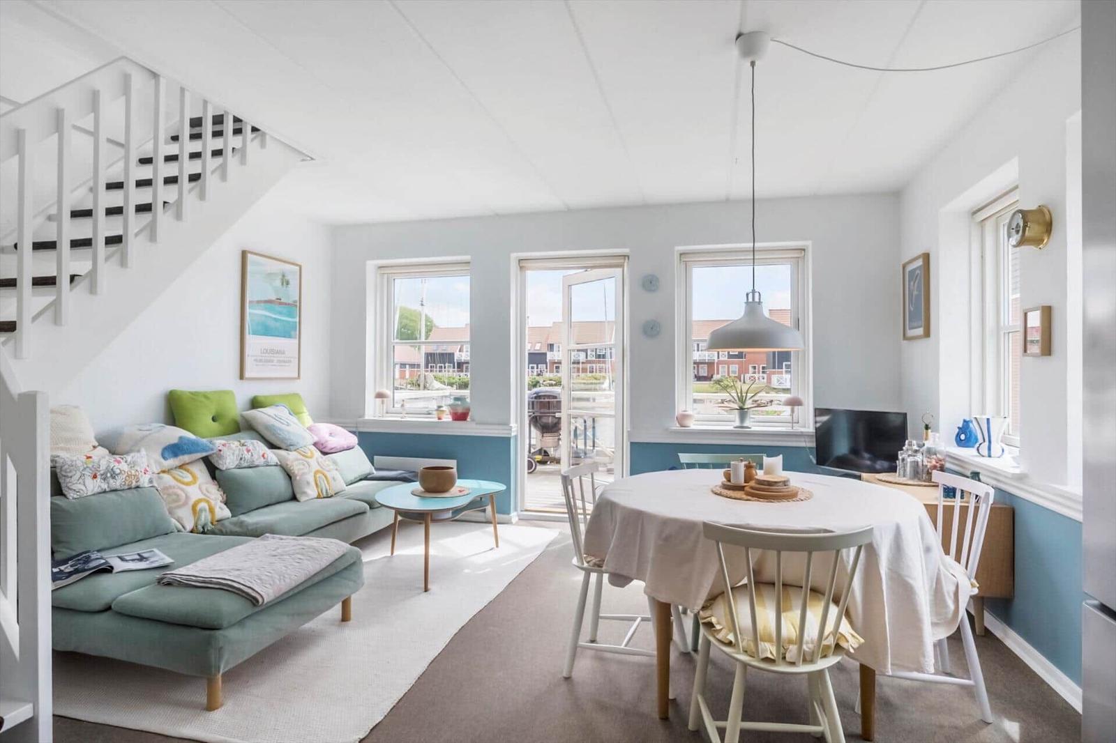 Wohn- und Essbereich mit Sofa, Tisch und Stühlen. Hintergrund: Fenster und Treppe.