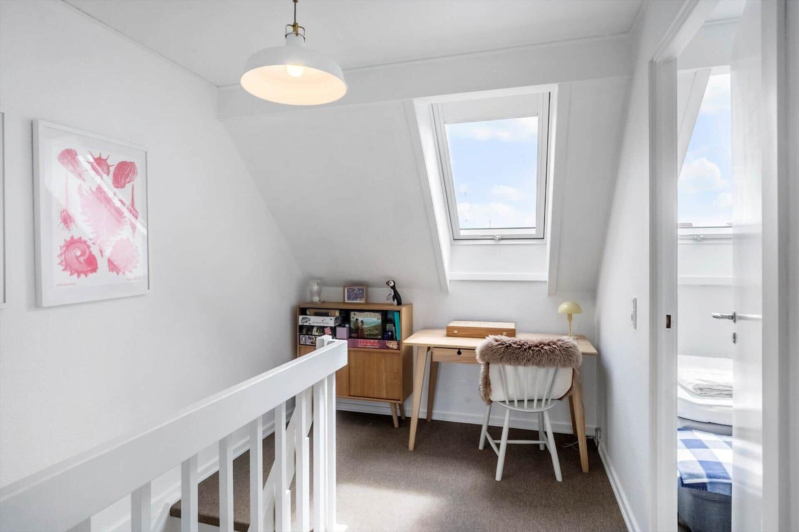 Ein Zimmer mit Schreibtisch, Fenster und Wandbild. Durchgang zu einem Schlafbereich.