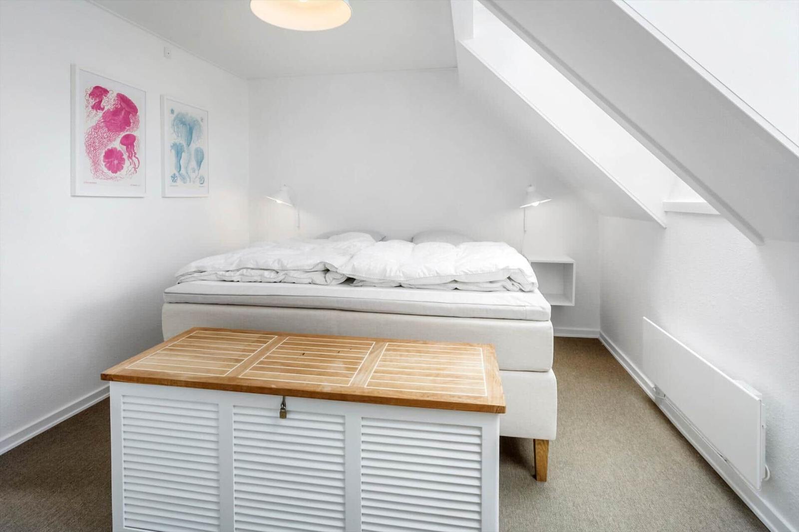 Schlafzimmer mit Dachschrägen, Bett, Holzbox und Wandbildern.