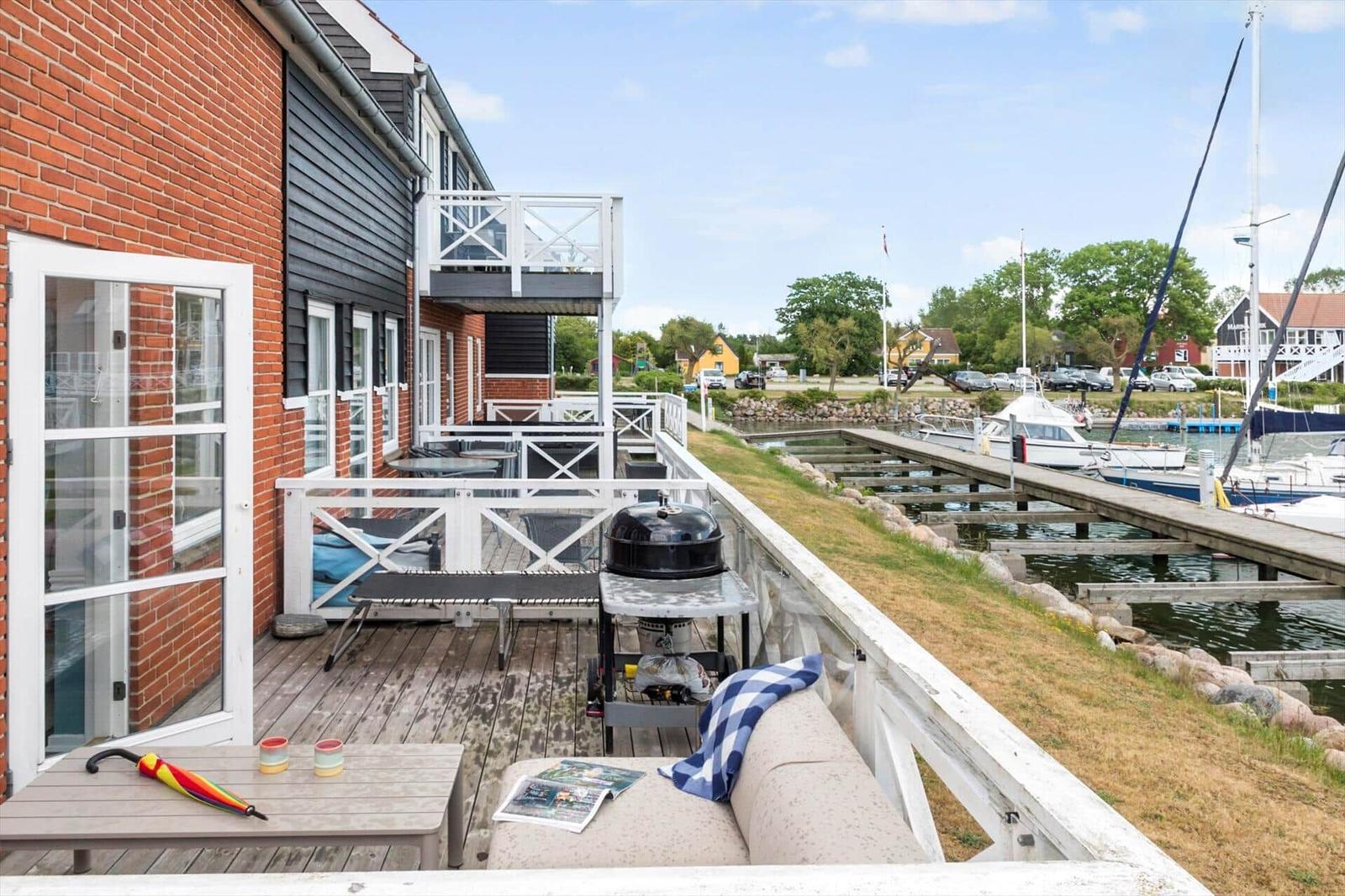 Terrasse mit Grill und Sofa, Blick auf Hafen mit Booten.