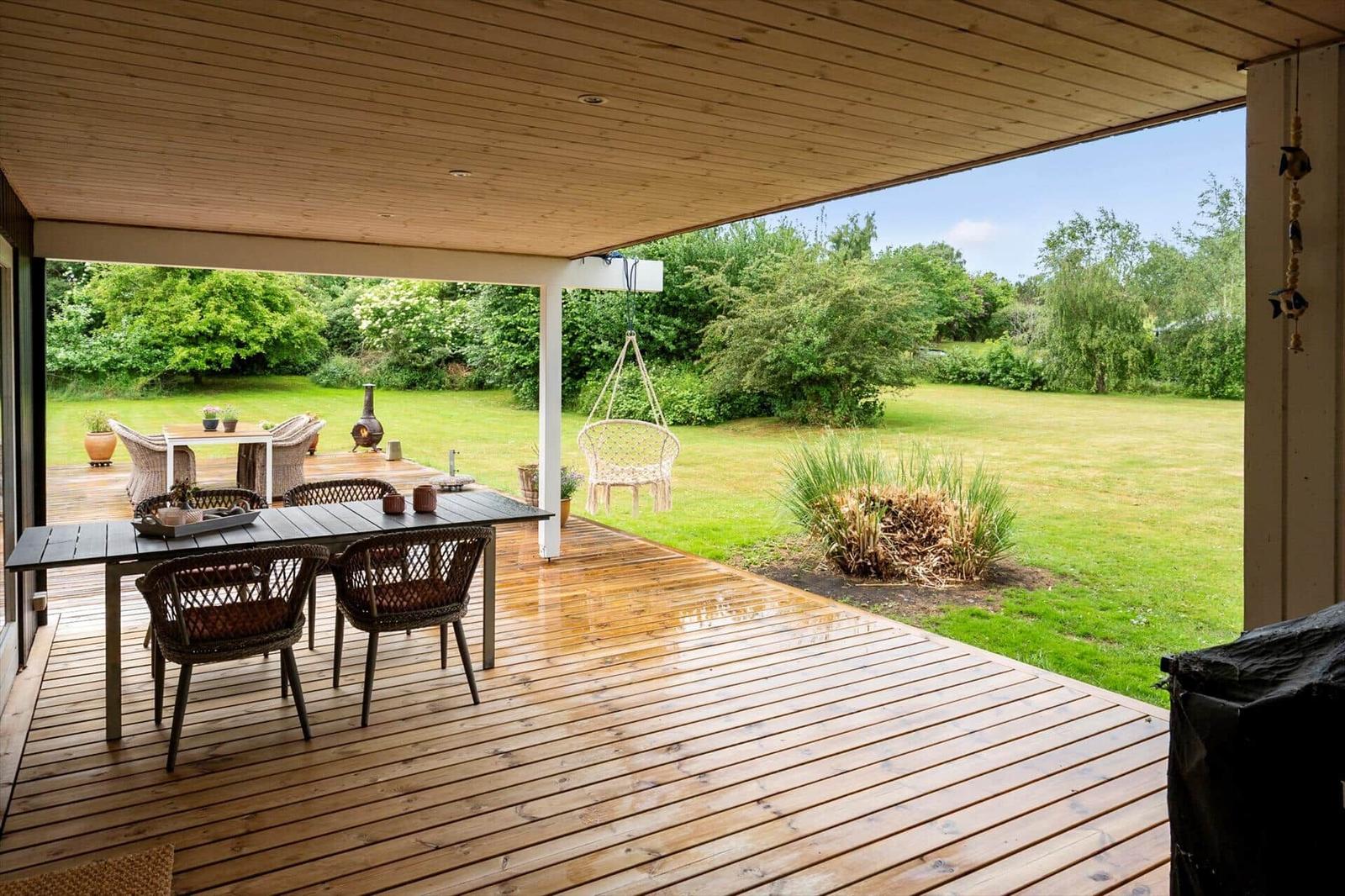 Terrasse mit Tisch, Stühlen und Schaukel. Blick auf grünen Garten und Bäume.
