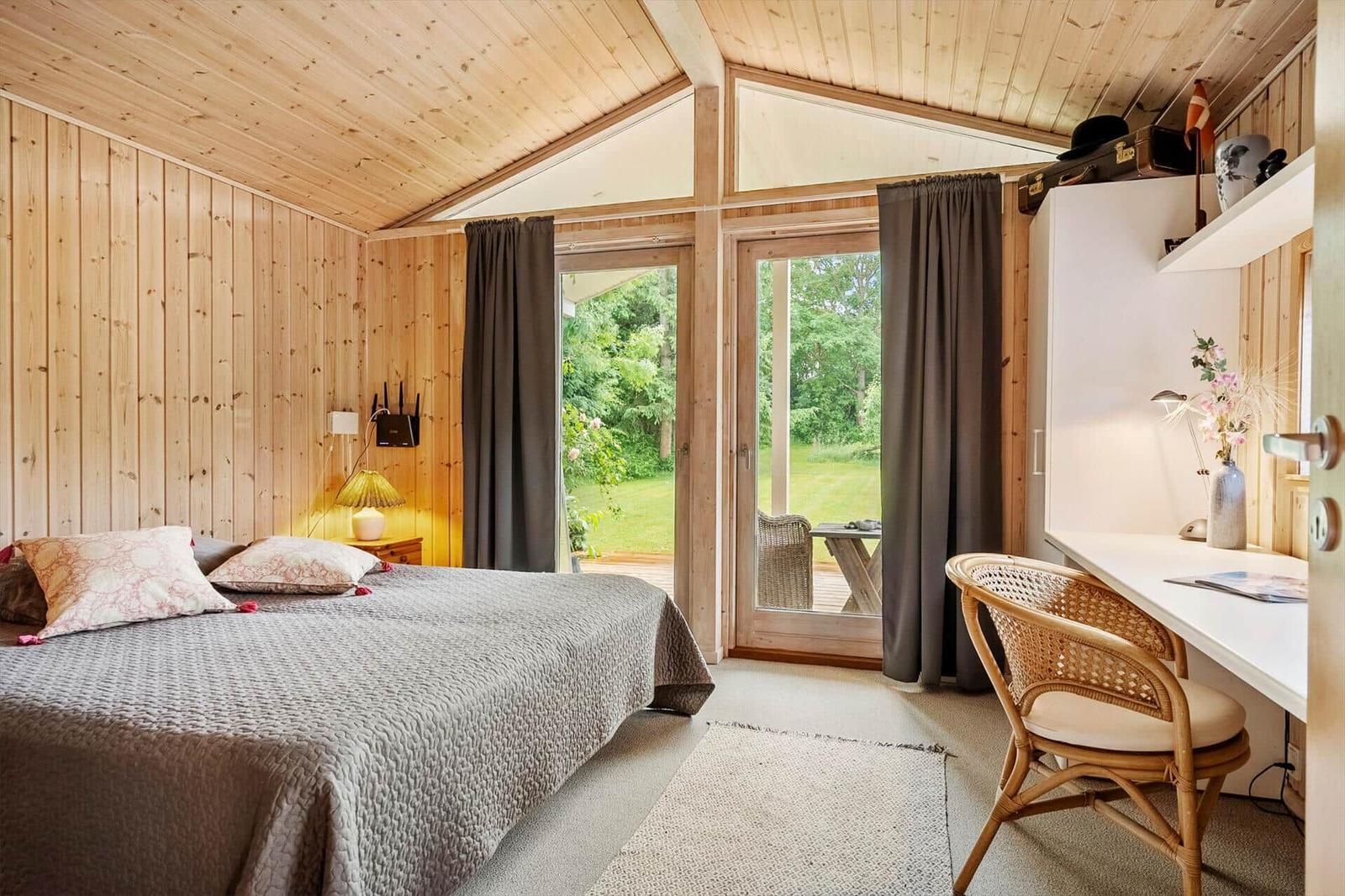Schlafzimmer mit Holzwand, Bett, Schreibtisch und Blick auf Garten.