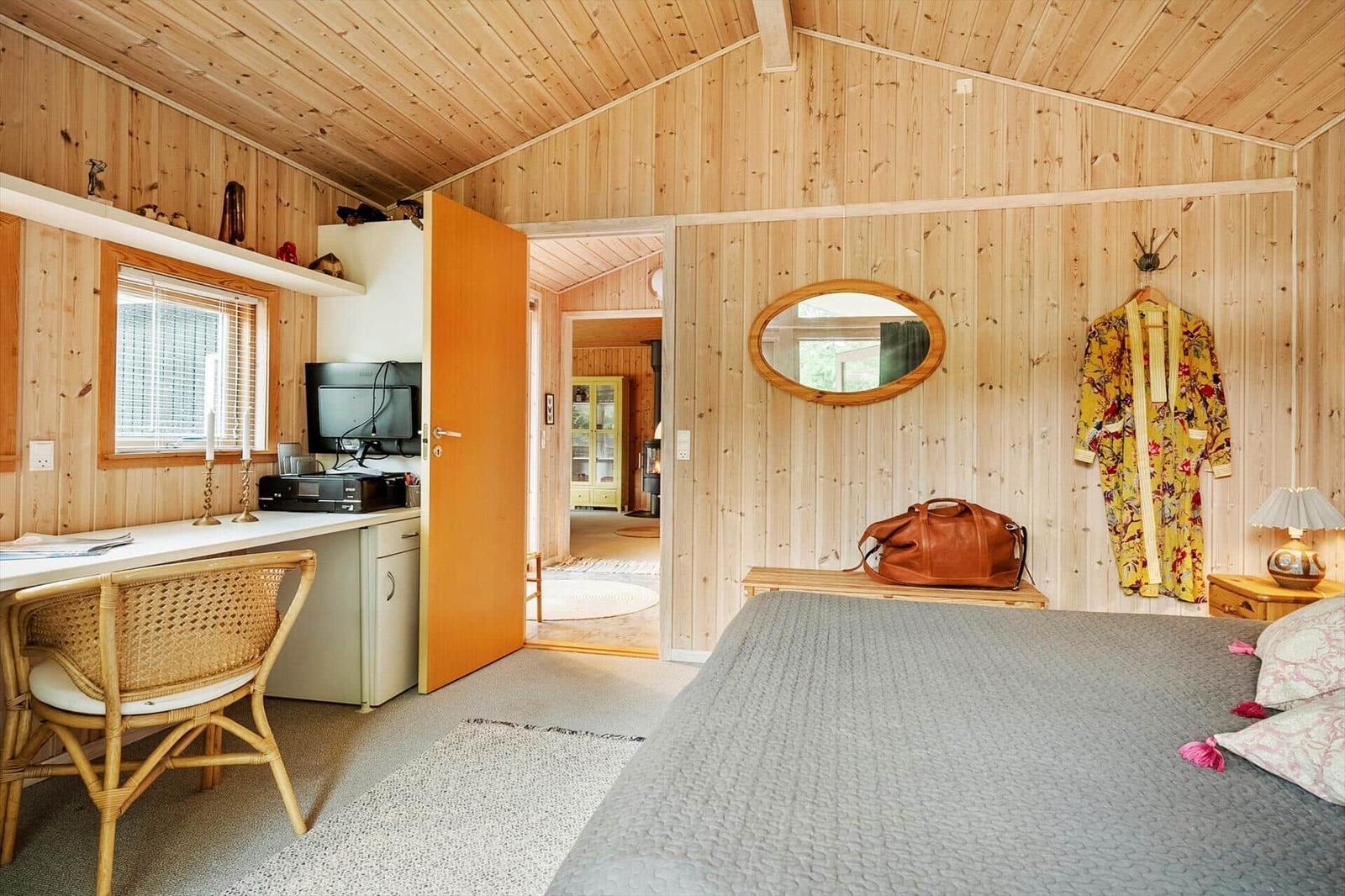Schlafzimmer mit Holzwand, Bett, Schreibtisch und Blick in den Flur.