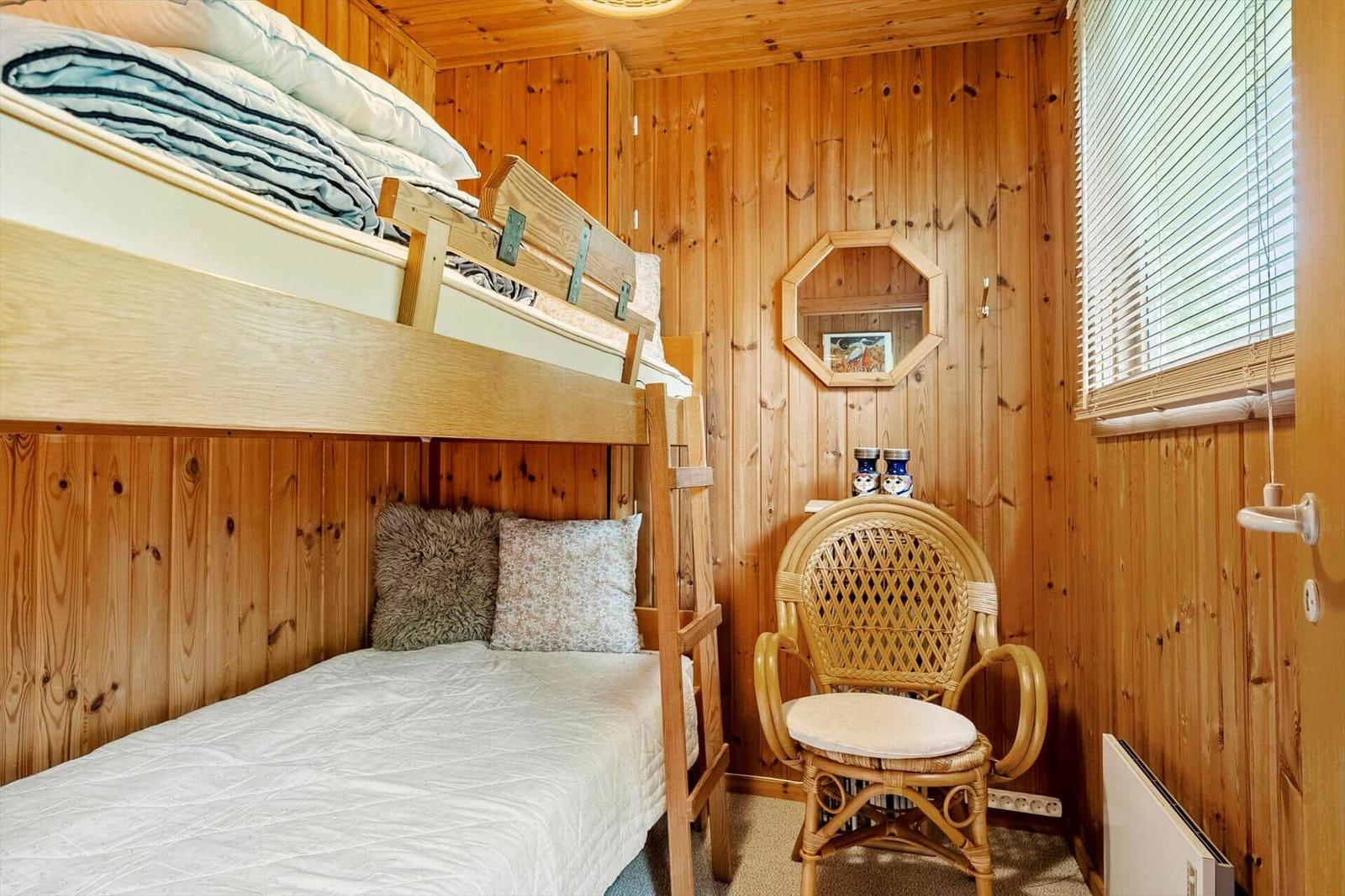Zimmer mit Doppelstockbett, Stuhl und Holzwandverkleidung.